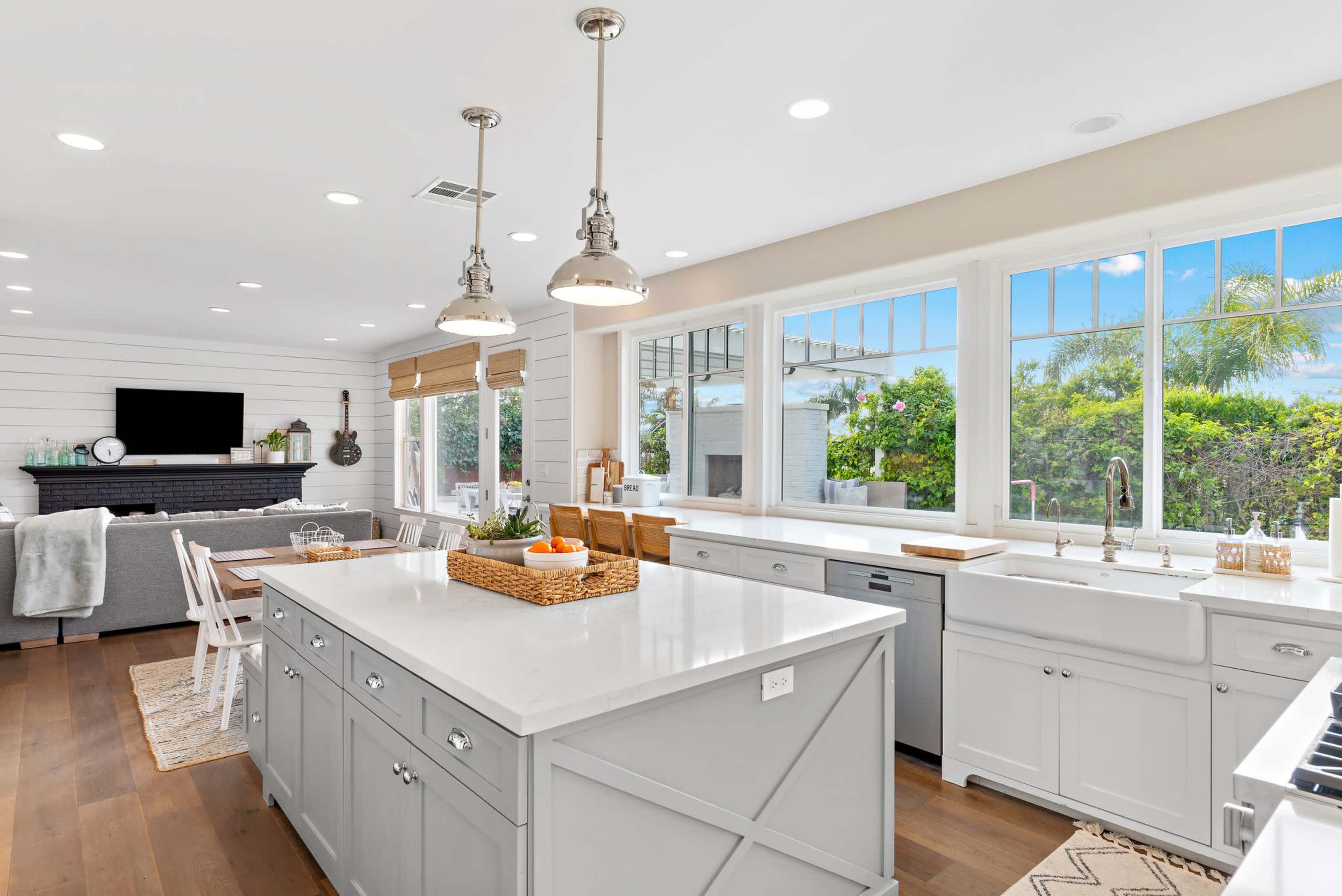 A modern kitchen with a large island, white cabinetry, stainless steel appliances, and large windows providing natural light and a view of the outdoors.