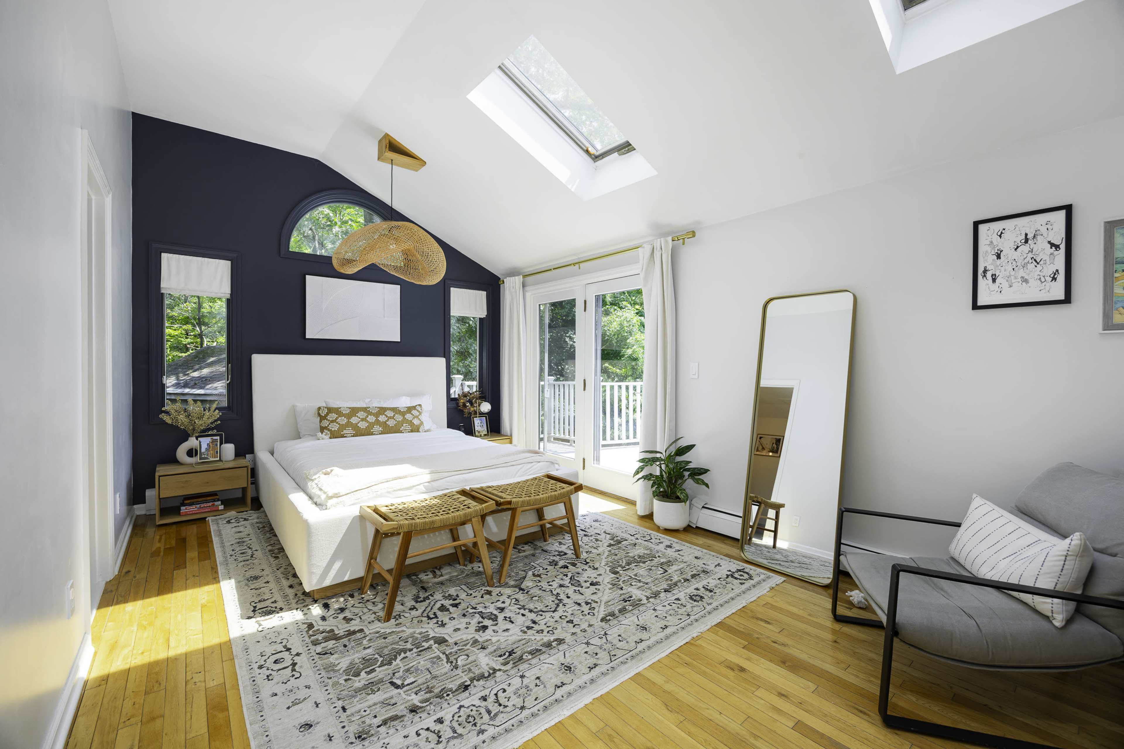 The room features a bed with a patterned blanket, a large mirror, a cozy seating area, and skylights letting in natural light.