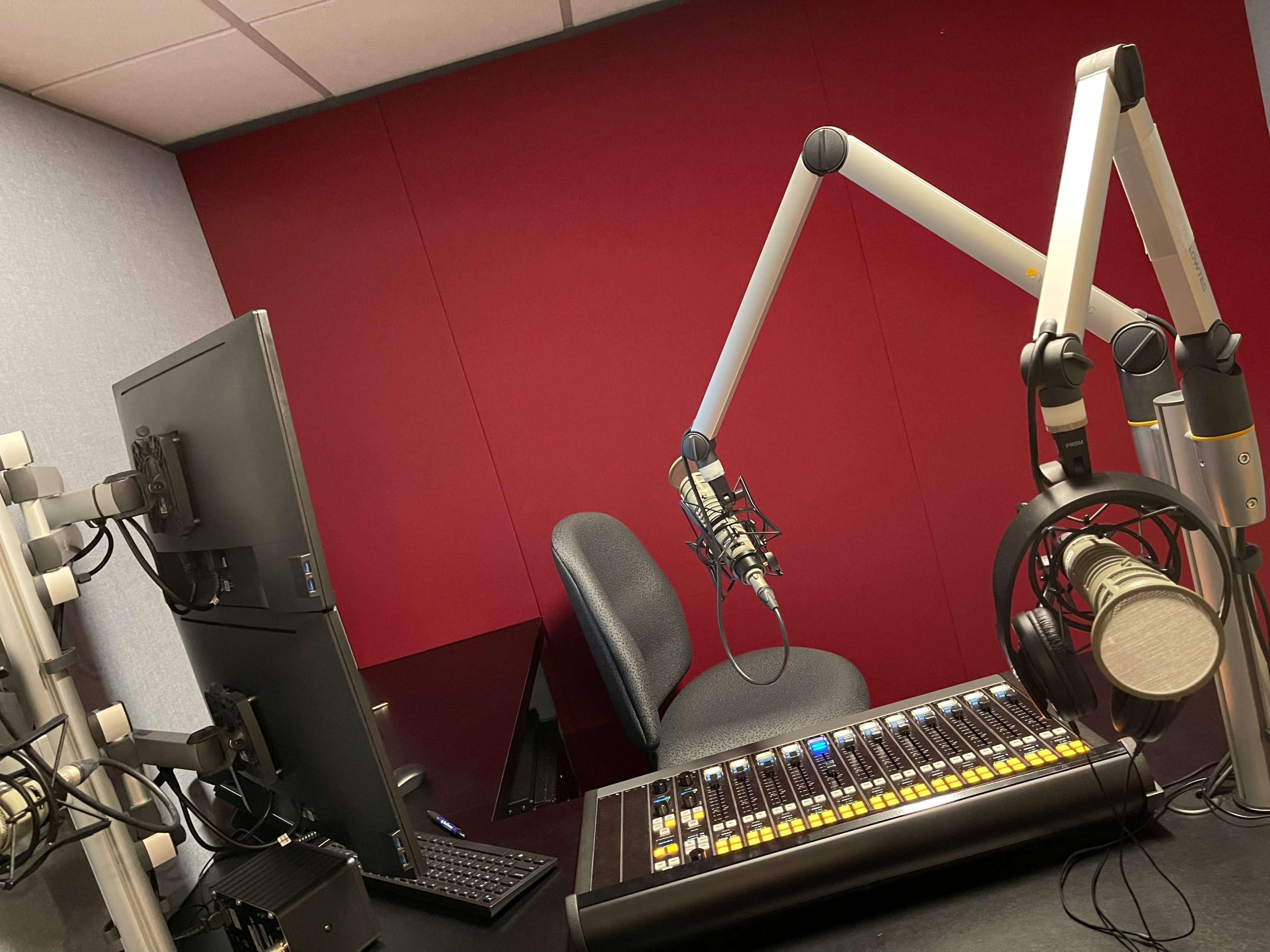 A radio studio setup featuring a computer monitor, a chair, and a mixing console with microphones and headphones.