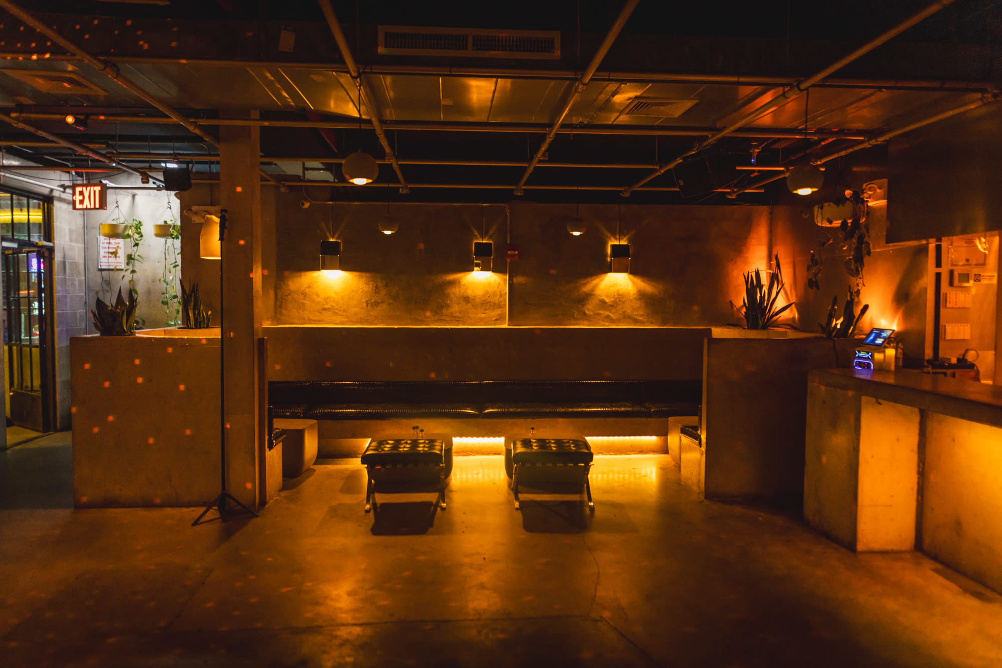 The image depicts a dimly lit lounge area with a concrete wall, a black bench, and two crates positioned on the floor.
