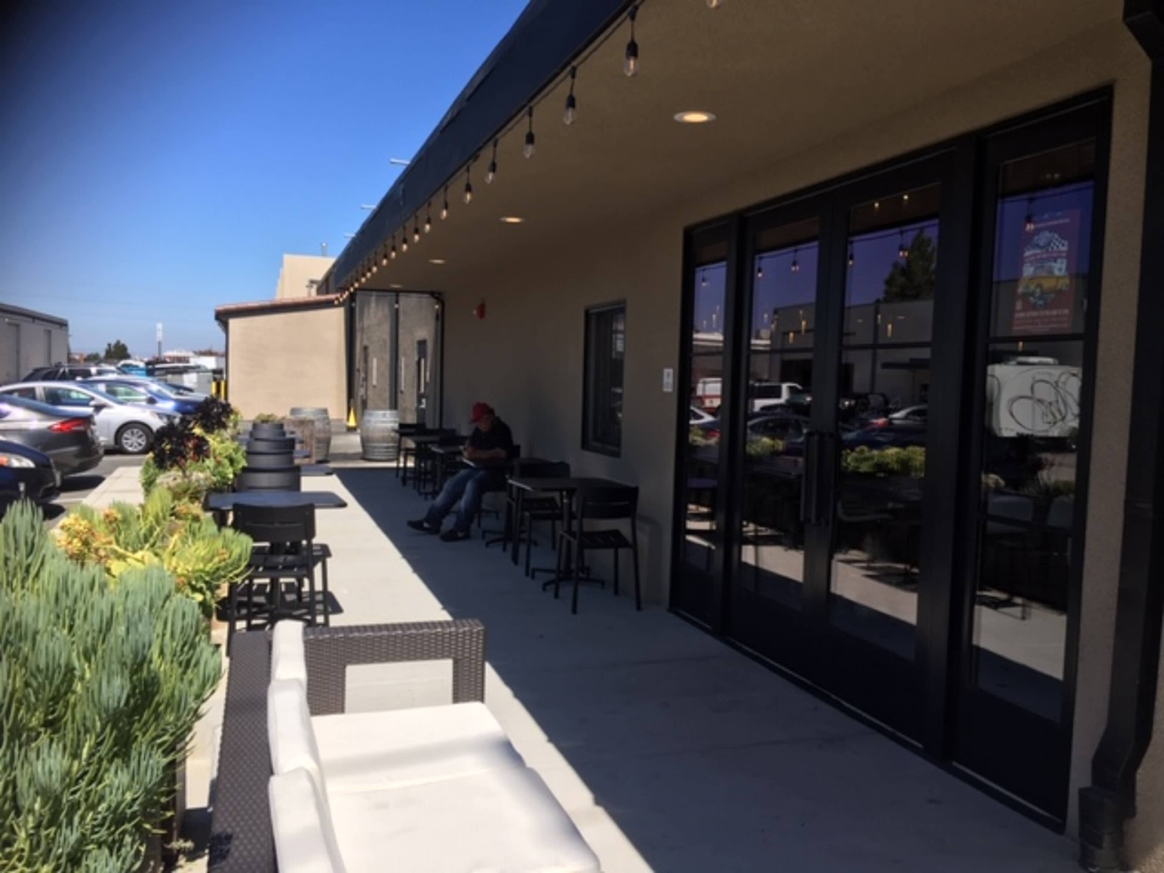 An outdoor seating area of a restaurant or café with several tables, chairs, and a person sitting alone near the entrance.
