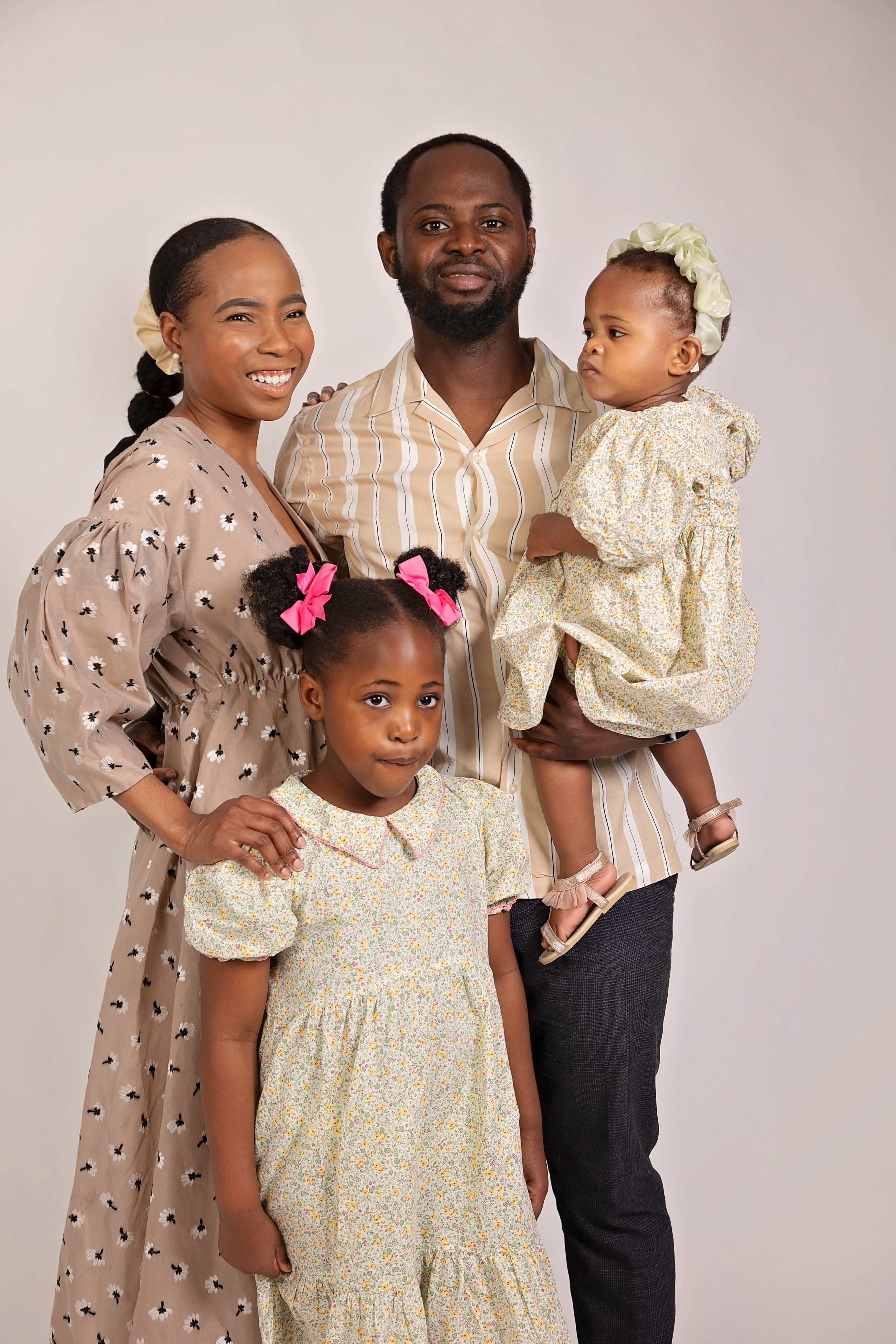 A family of four poses for a portrait, with two children in floral dresses, while the adults smile at the camera.