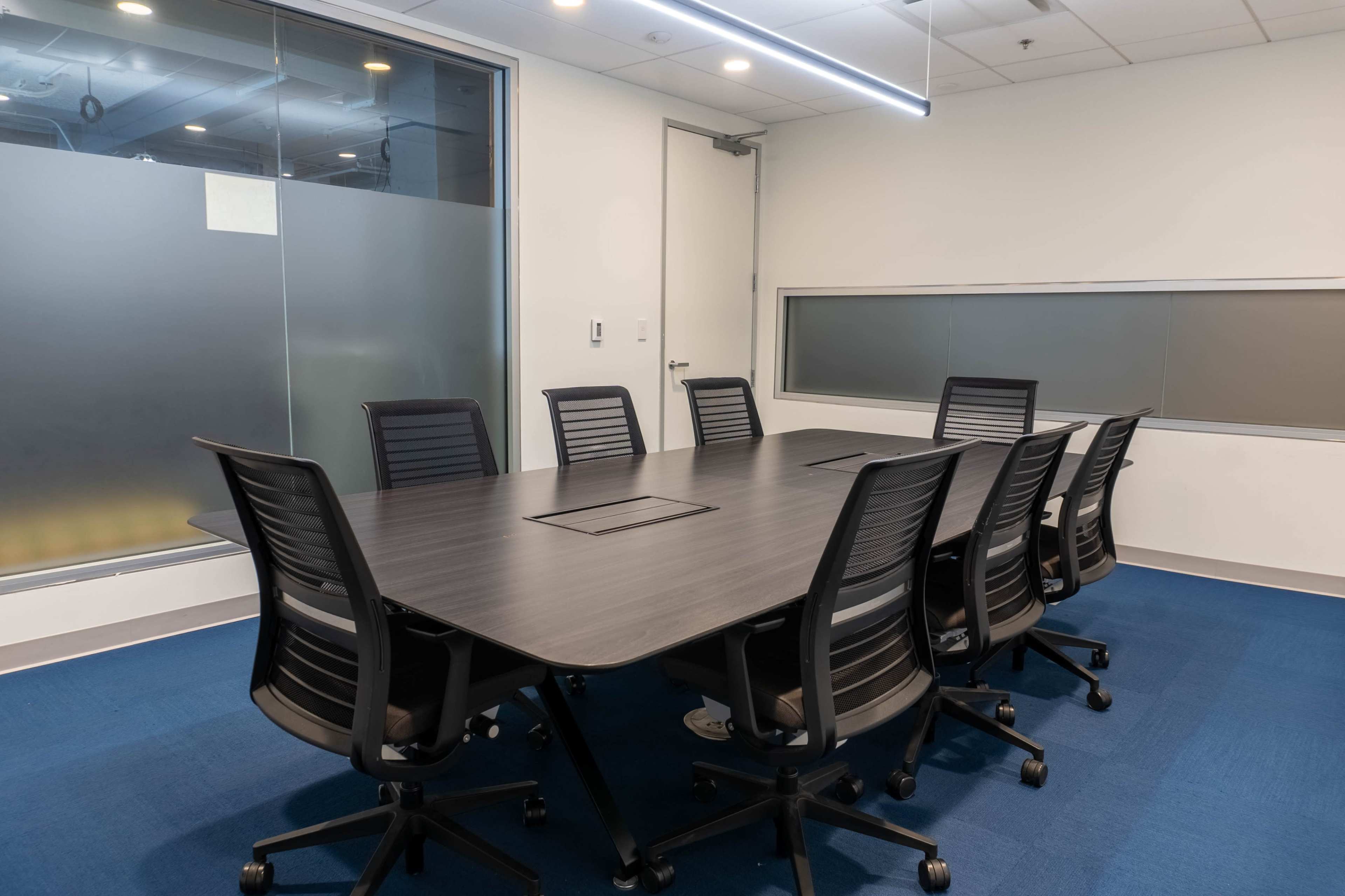 A modern conference room with a long rectangular table and eight black ergonomic chairs arranged around it.