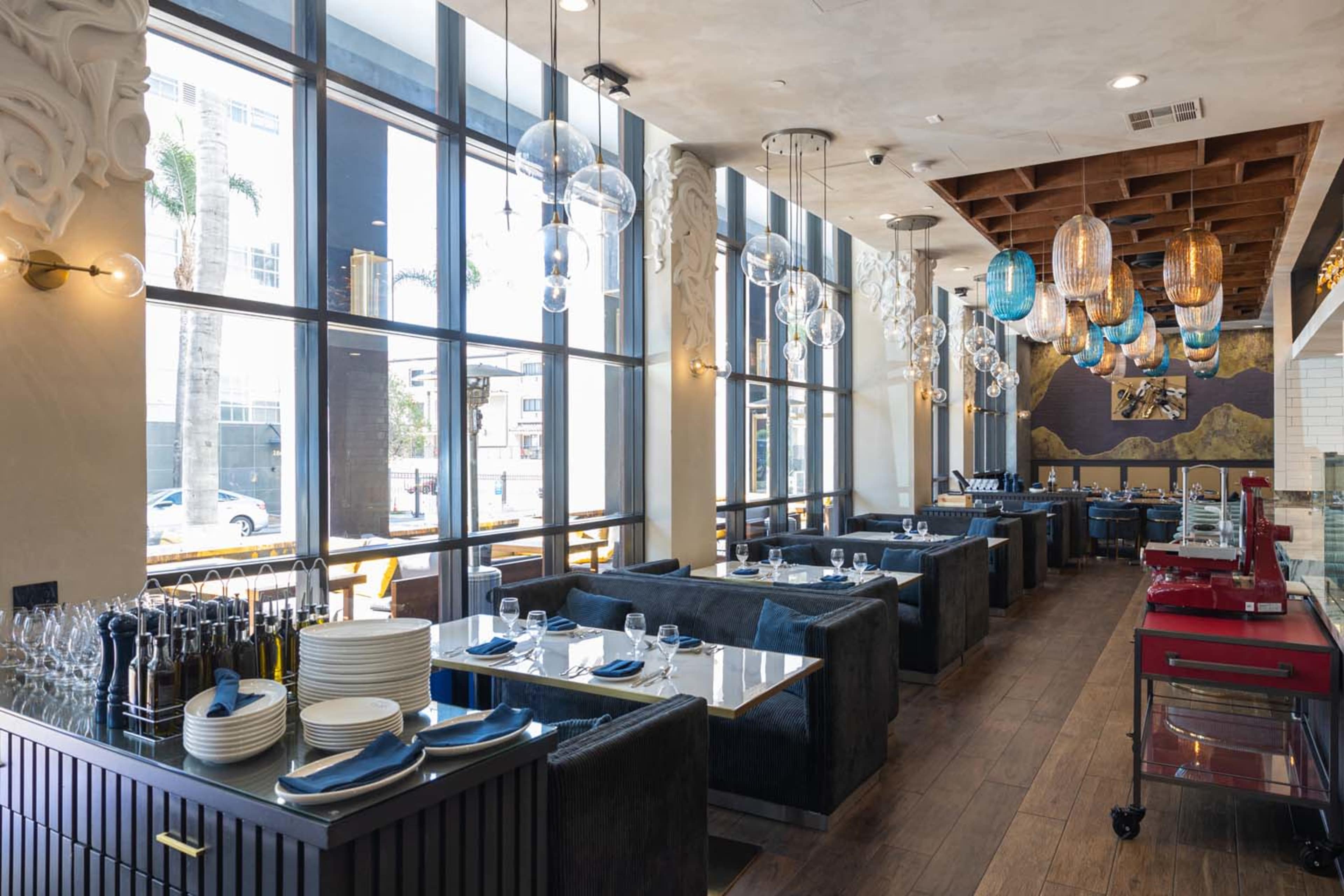 The image shows a modern restaurant interior with large windows, blue seating booths, and decorative hanging light fixtures.