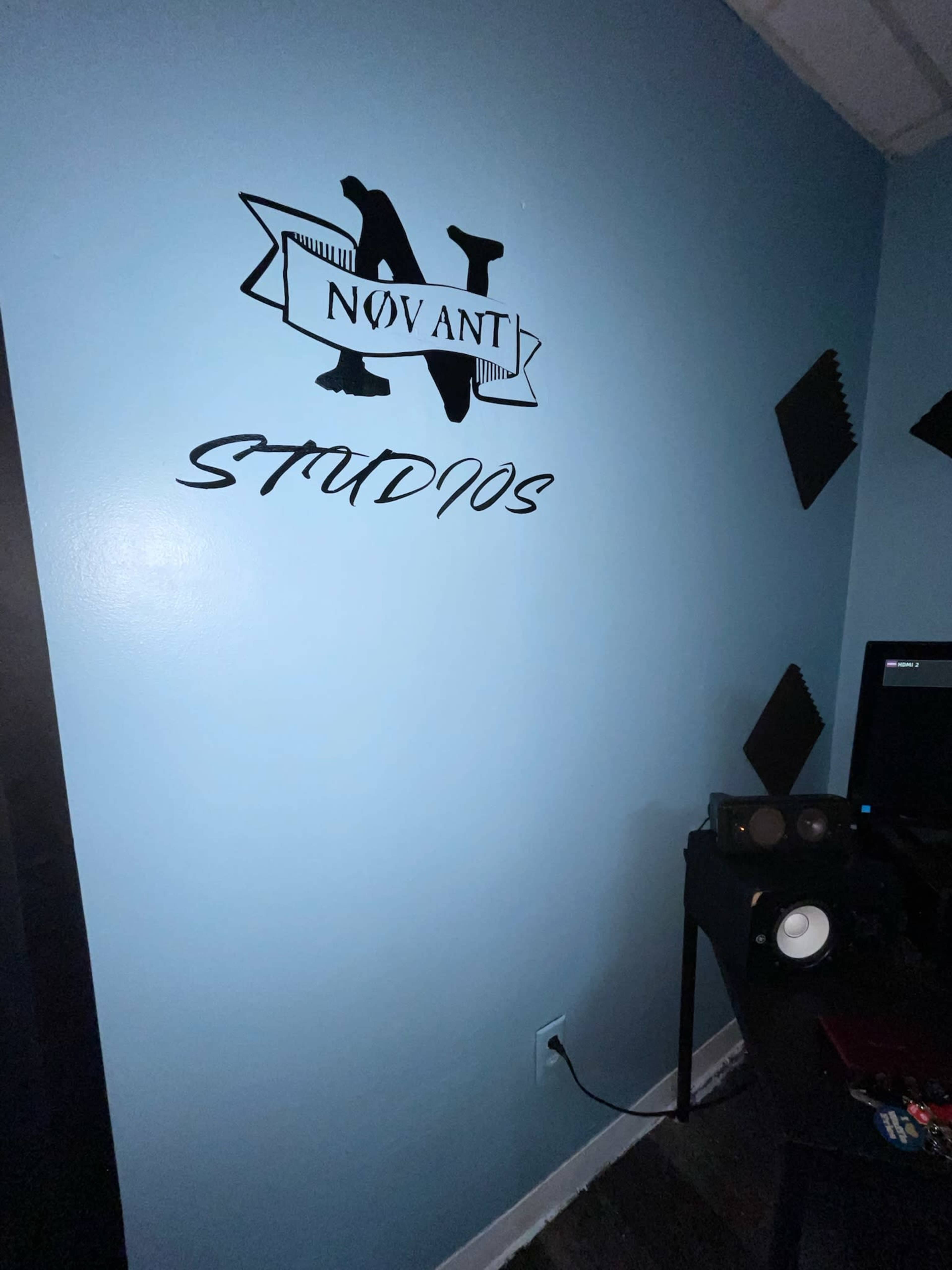 The image shows a blue wall featuring a black decorative sign that reads "NOVANT STUDIOS" above a small desk with audio equipment.