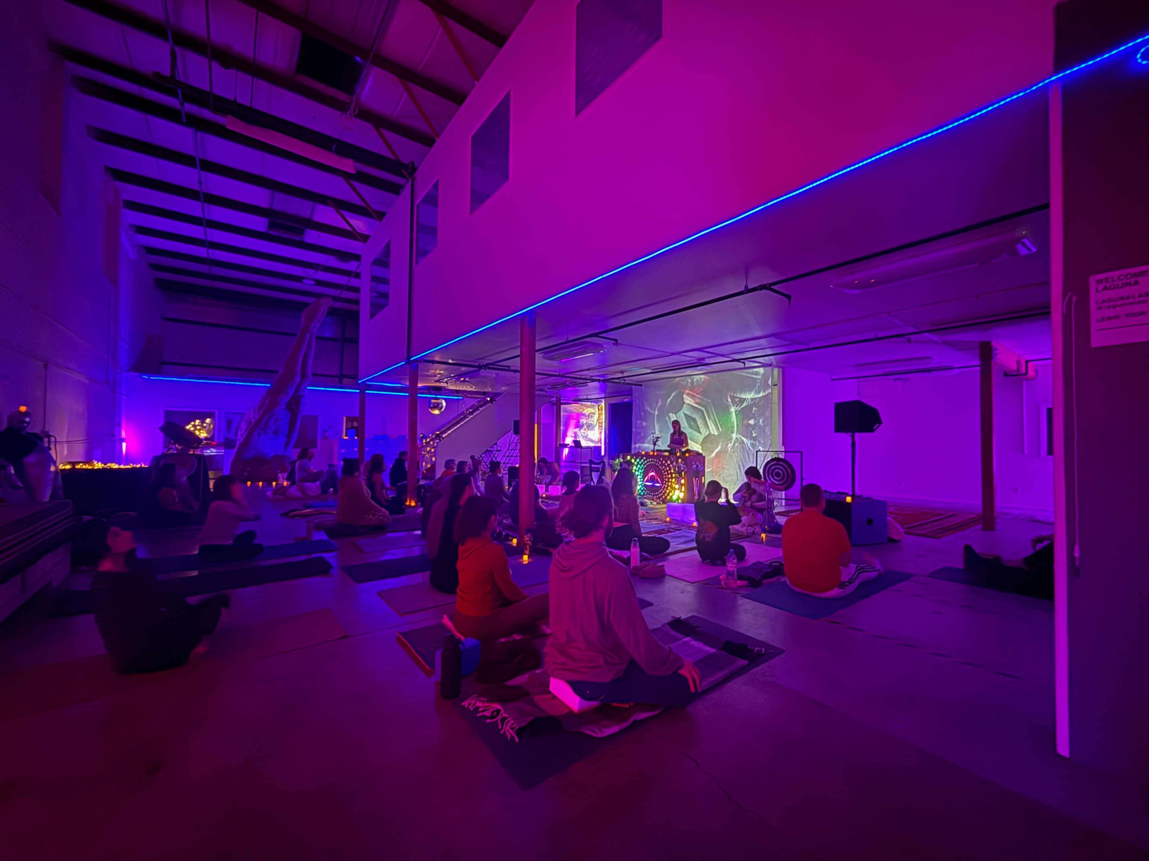 A group of attendees participates in a guided meditation session in a dimly lit room with purple lighting and a projection screen.