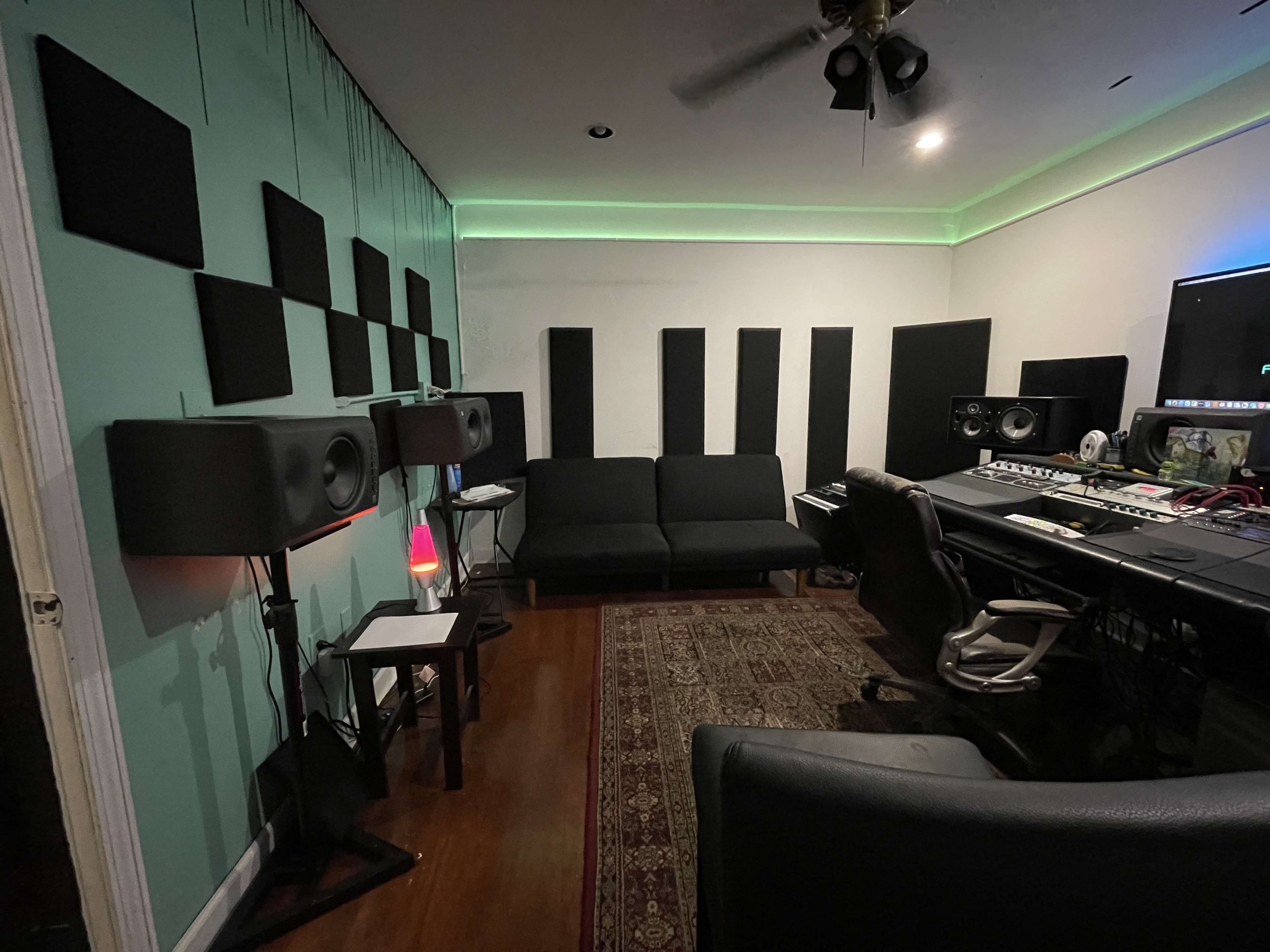 A music studio with soundproofing panels on the walls, a couch, and audio equipment arranged for recording.