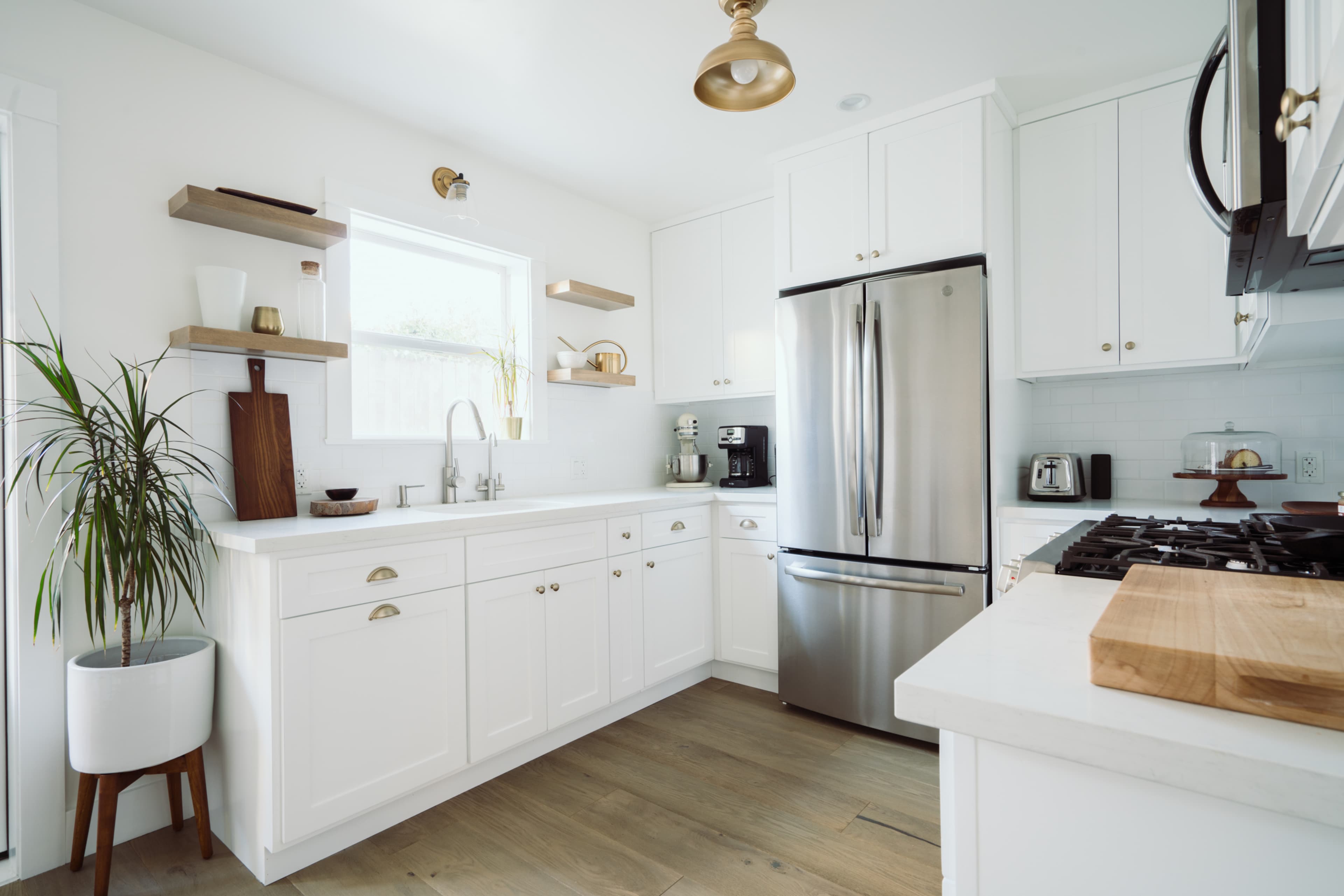 A bright kitchen features white cabinetry, stainless steel appliances, and wooden accents, with a window allowing natural light to illuminate the space.