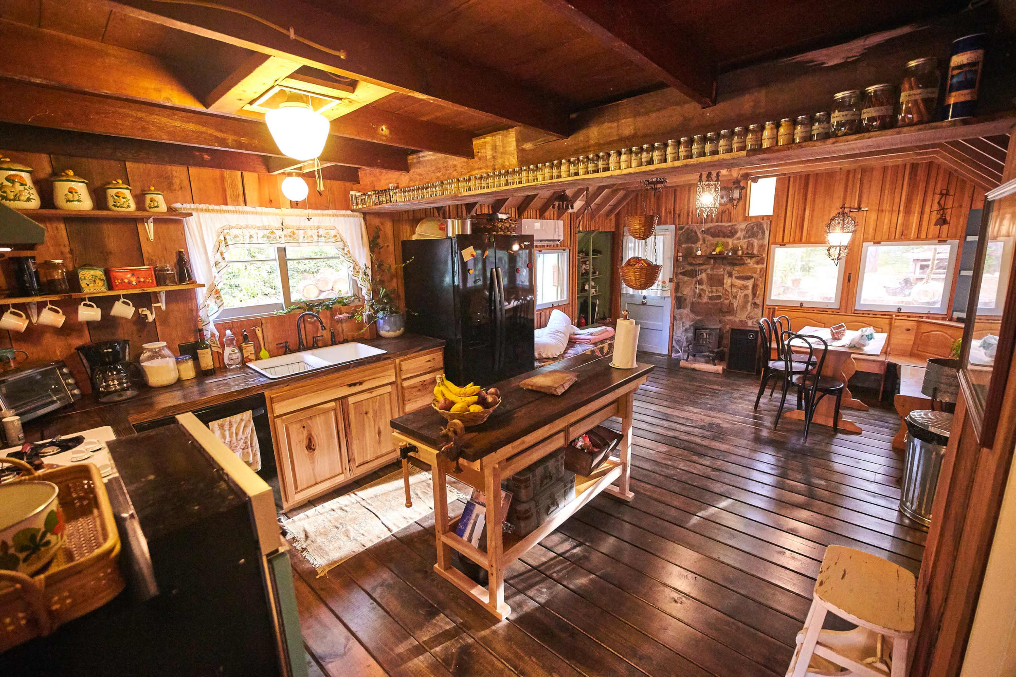 A rustic kitchen with wooden cabinets, a black refrigerator, and a central island, all set in a warmly lit, cozy space featuring wooden floors and vintage decor.