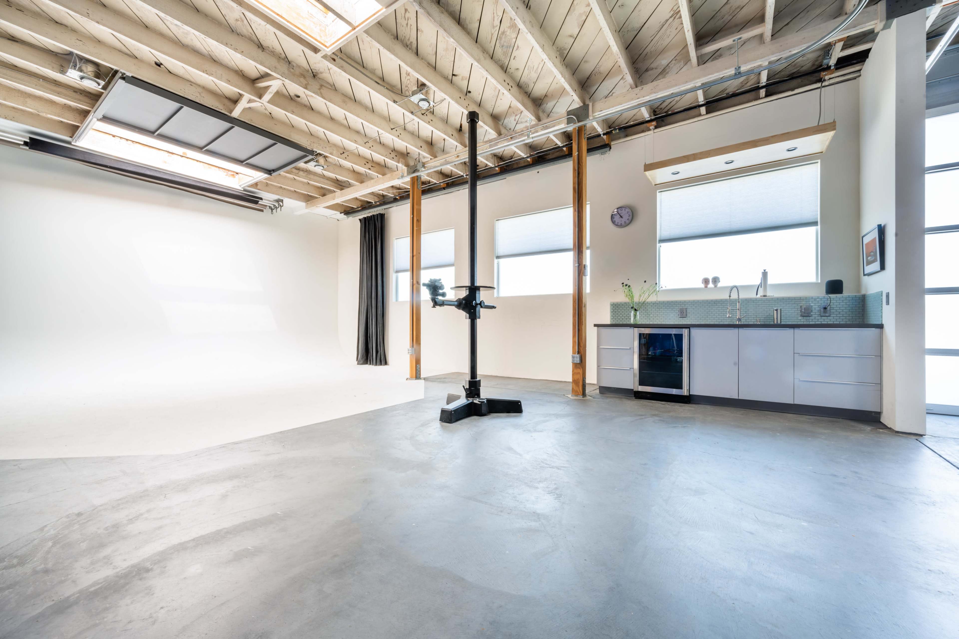 A spacious, empty studio with polished concrete floors, large windows, and a kitchenette area.