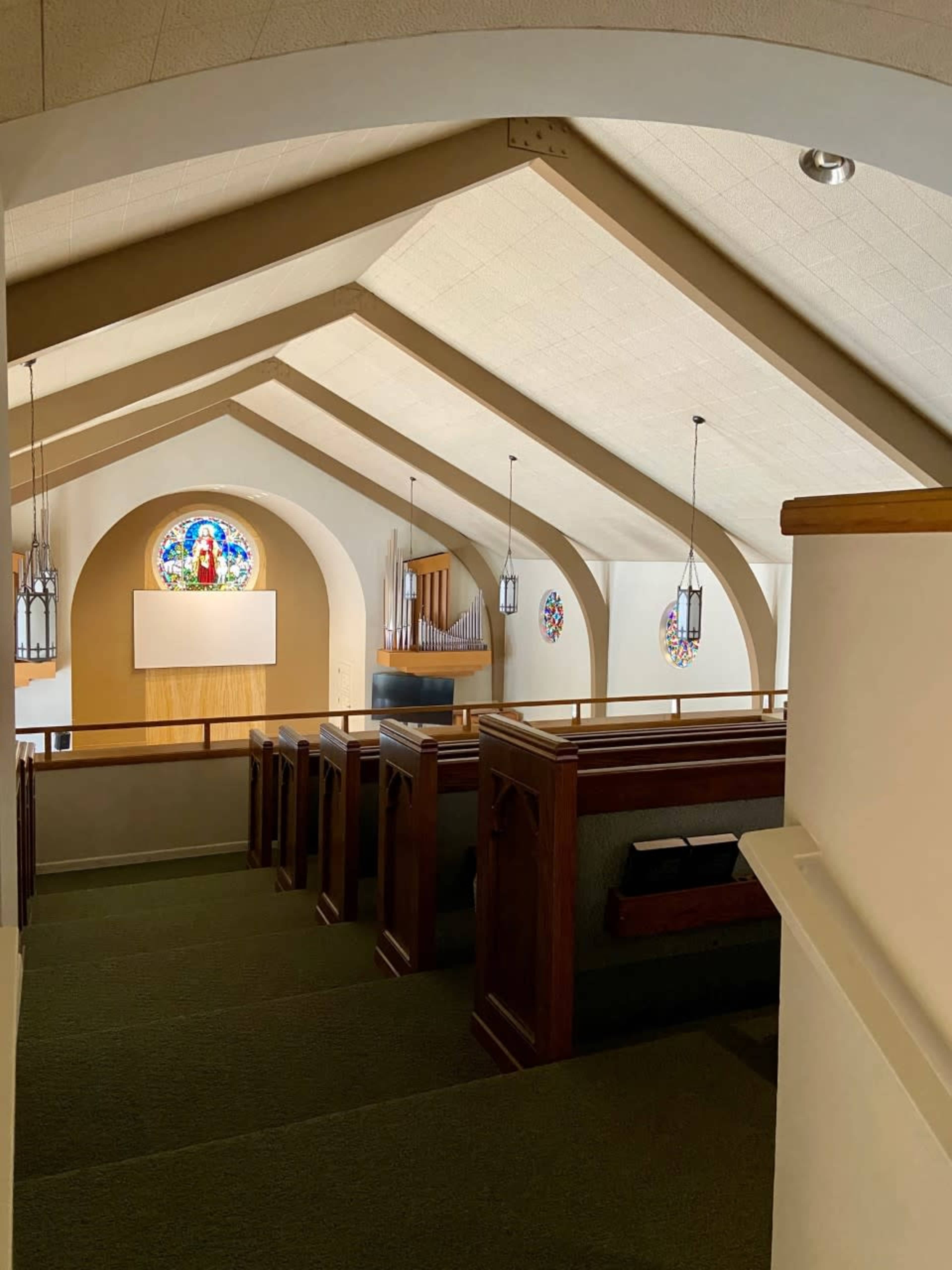 The interior of a church featuring wooden pews, a large decorative window, and an organ in the background.