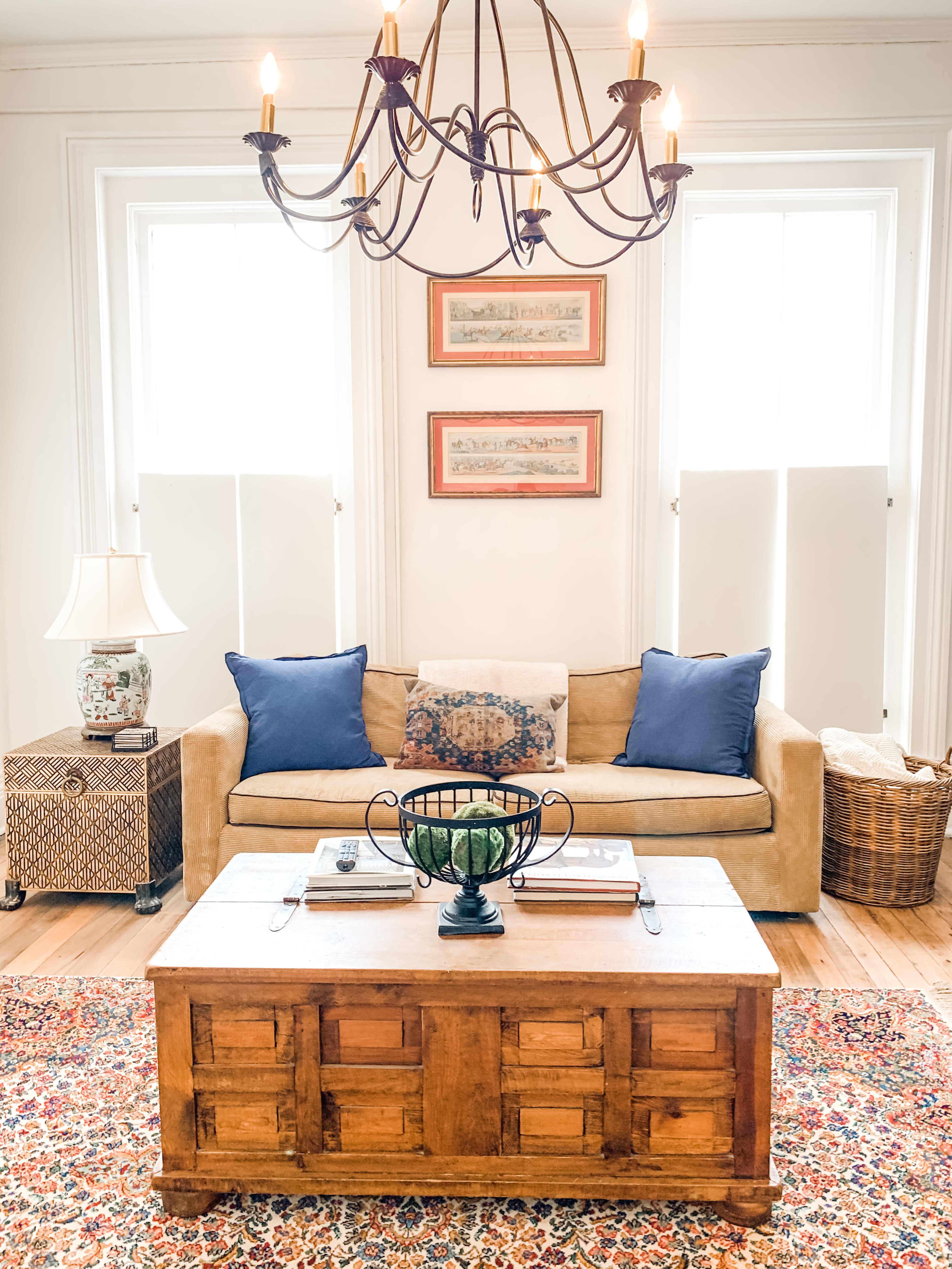 A cozy living room featuring a beige sofa with blue pillows, a wooden coffee table, and a decorative rug under a chandelier.