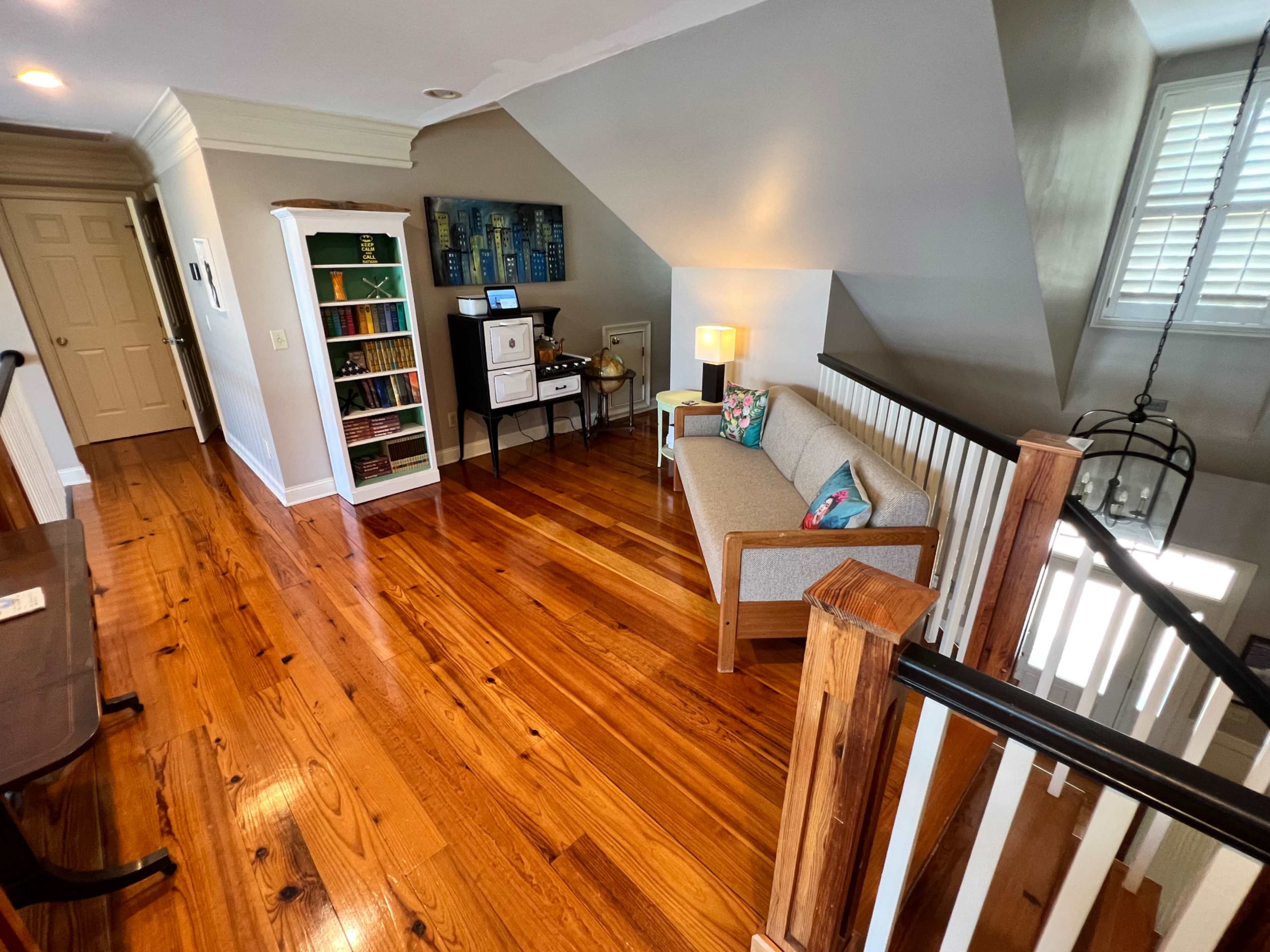 A well-lit hallway features polished wooden floors, a small sofa, a lamp, and a bookshelf against the wall.