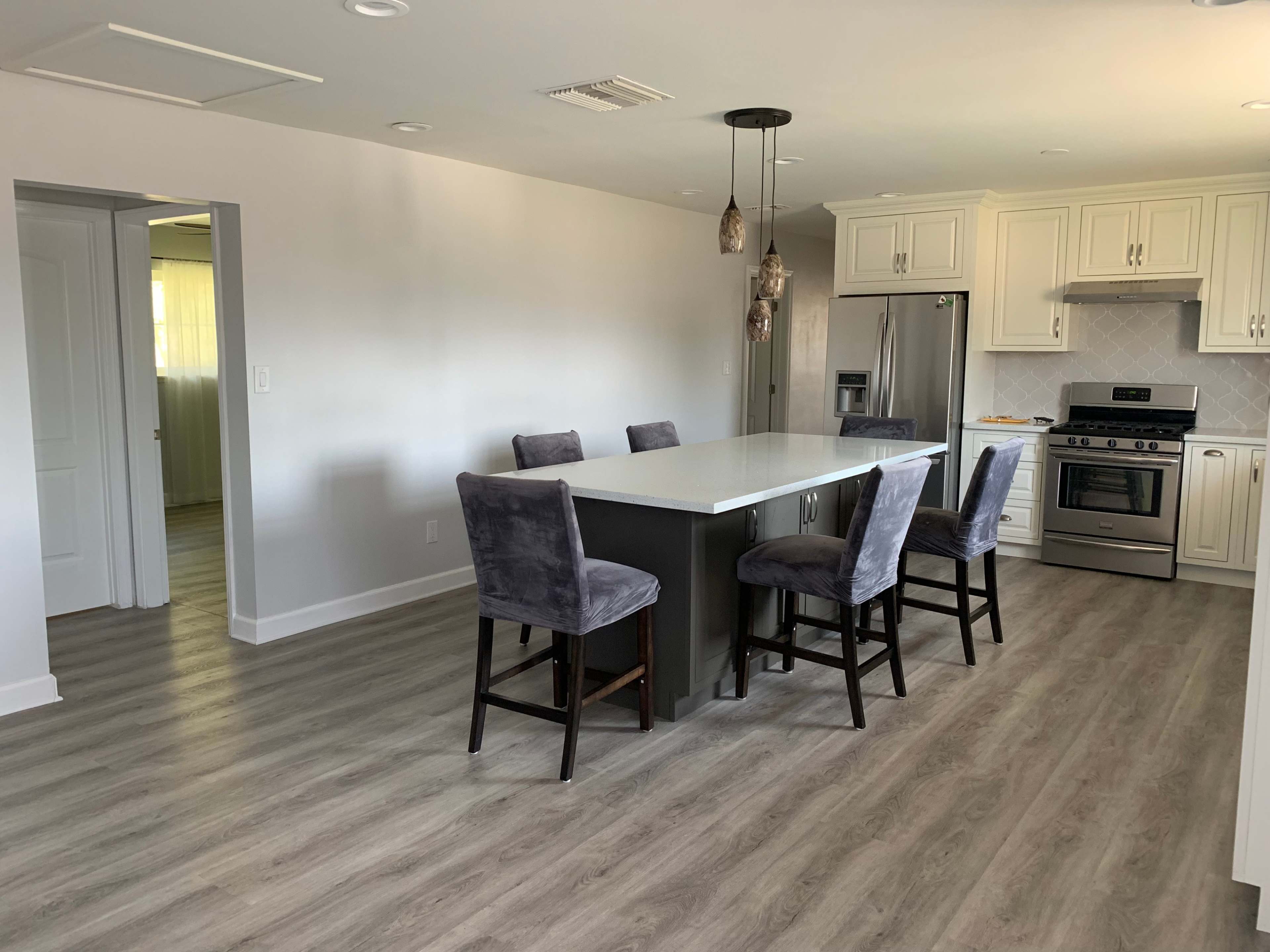 A modern kitchen features a central island with bar stools, stainless steel appliances, and light-colored cabinetry.