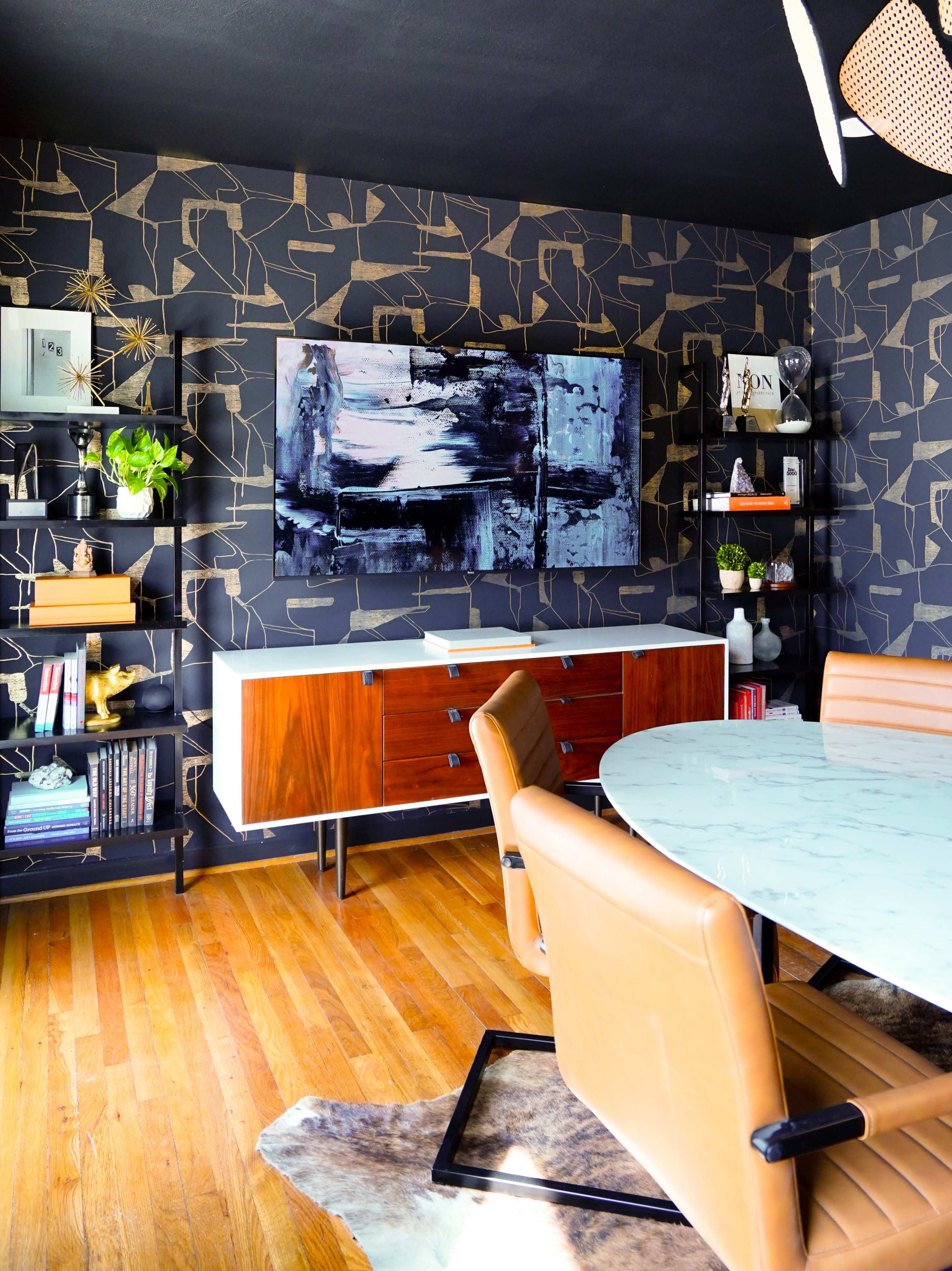 The image features a modern conference room with a marble-topped circular table, brown leather chairs, and a large wall-mounted television above a wooden storage cabinet, set against a patterned dark wallpaper.