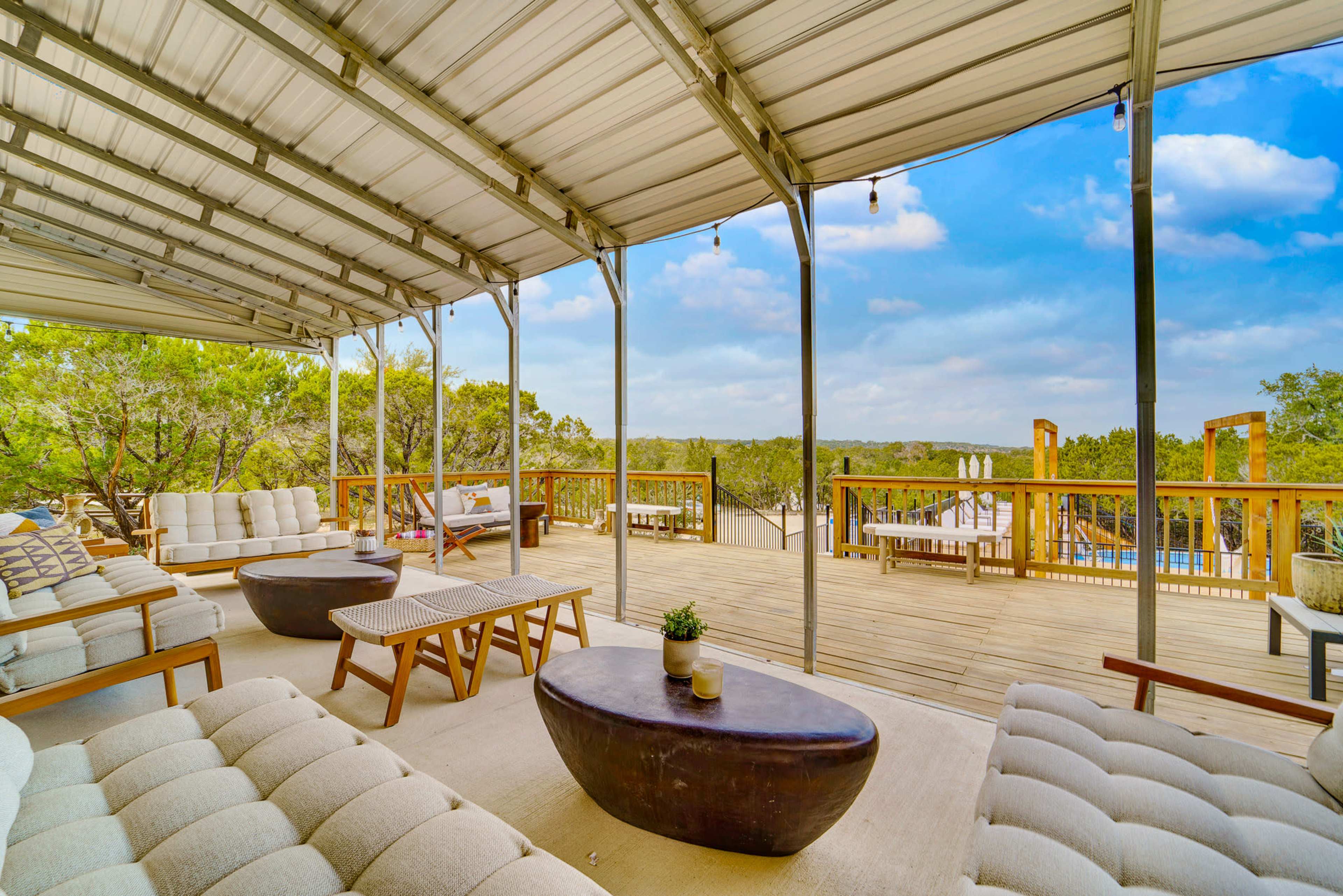 The image shows a spacious outdoor deck with modern seating arrangements and a view of surrounding trees and a distant landscape.
