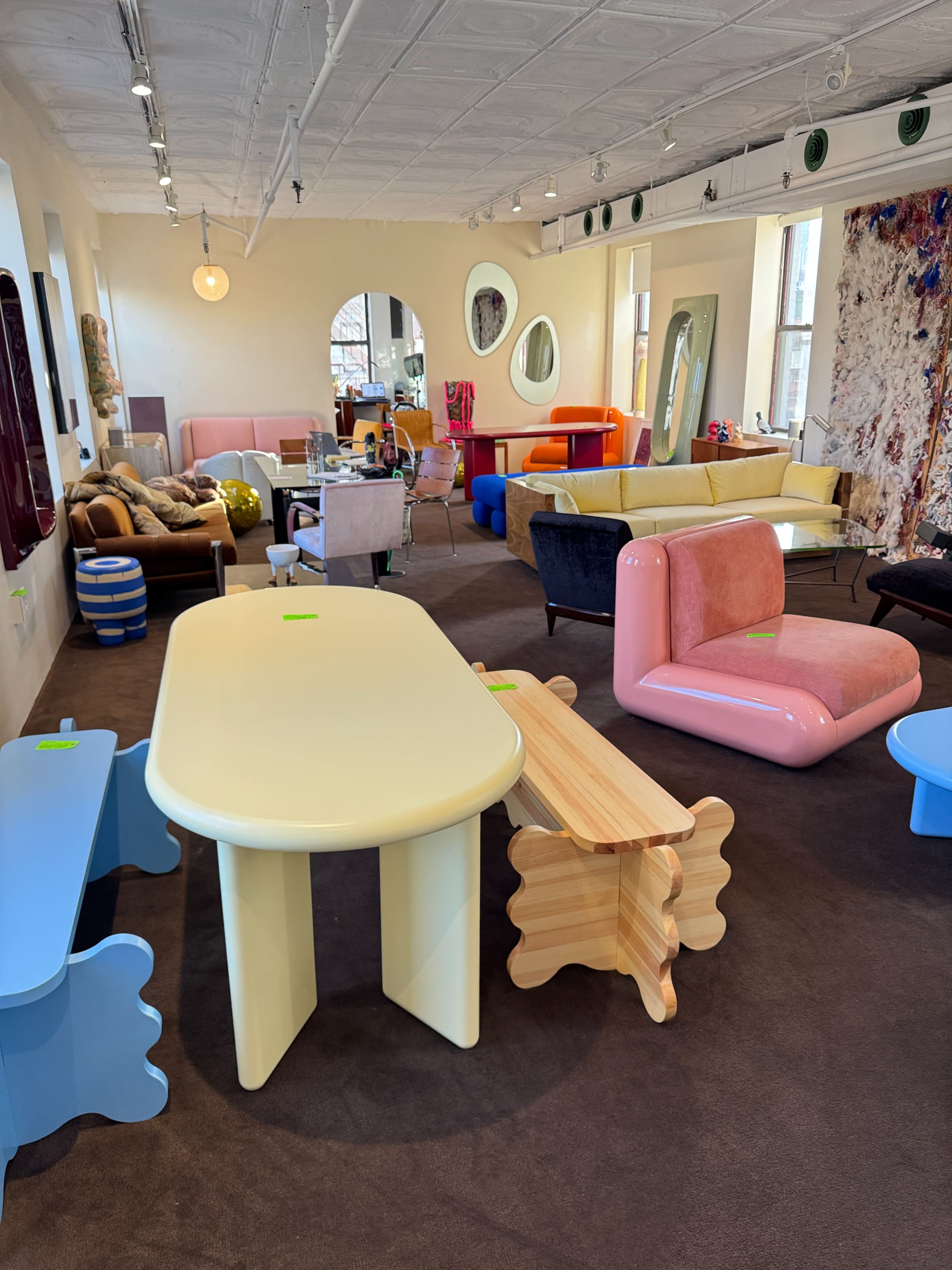 The image shows a vibrant furniture showroom filled with various colorful sofas, tables, and decorative items arranged in a spacious setting.