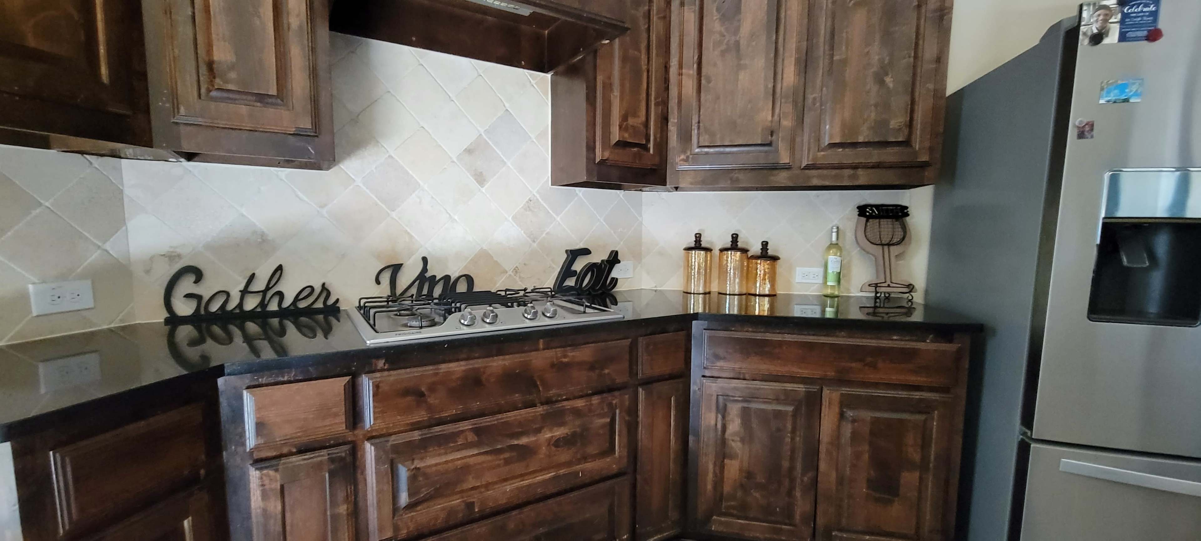 A kitchen with wooden cabinets, a gas stovetop, a black countertop, and decorative items on the counter.