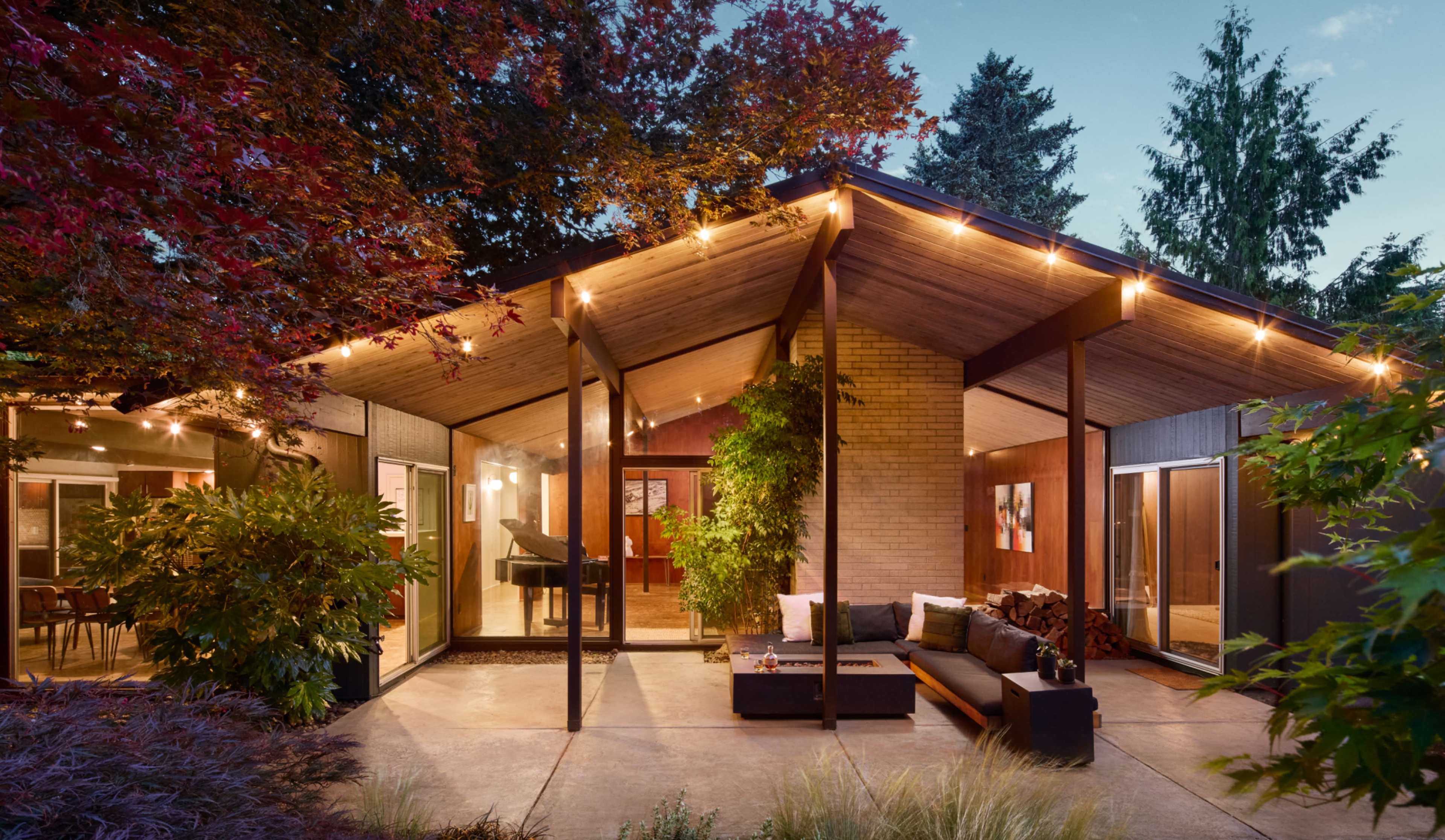A modern home features a spacious porch area surrounded by trees and decorative lighting.