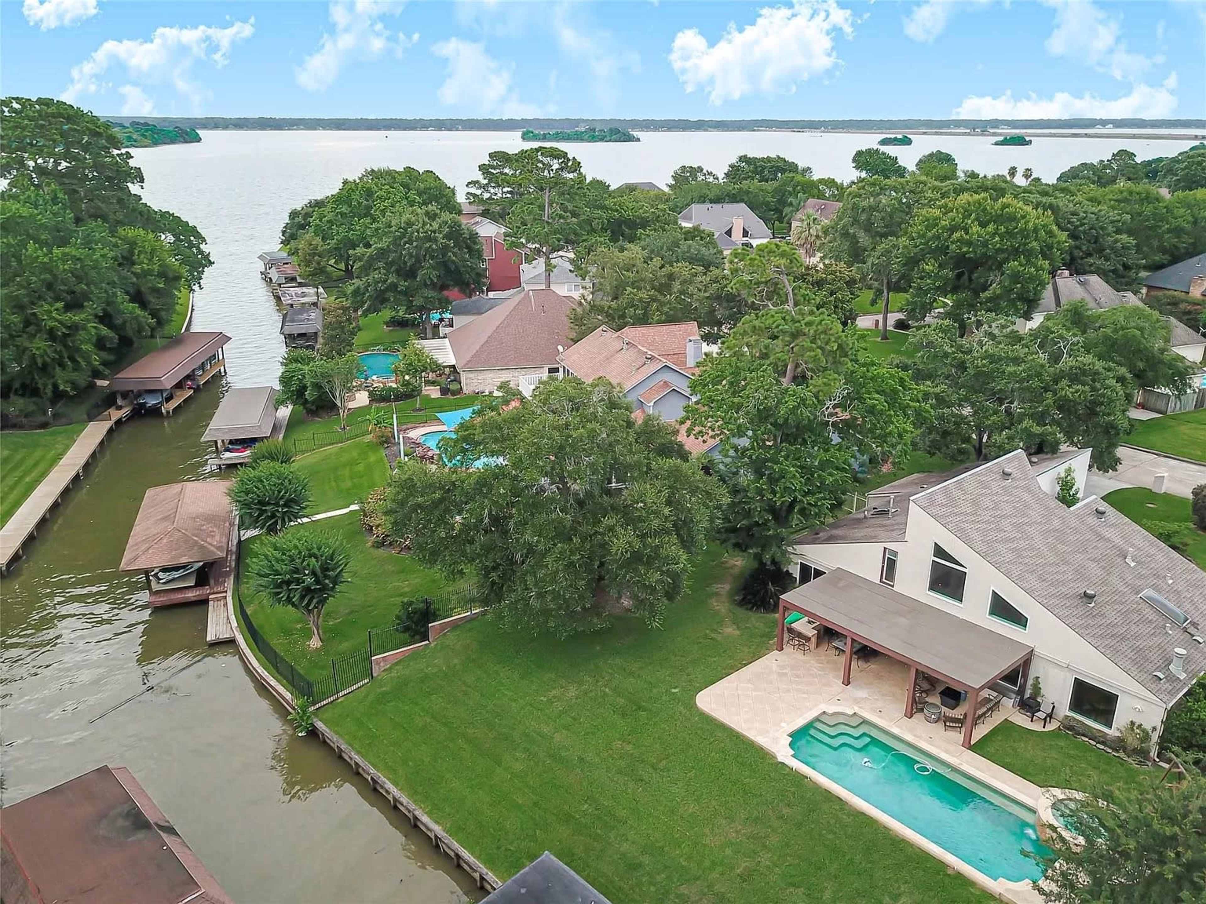 A residential area with homes, swimming pools, and a canal leading to a large body of water or lake.