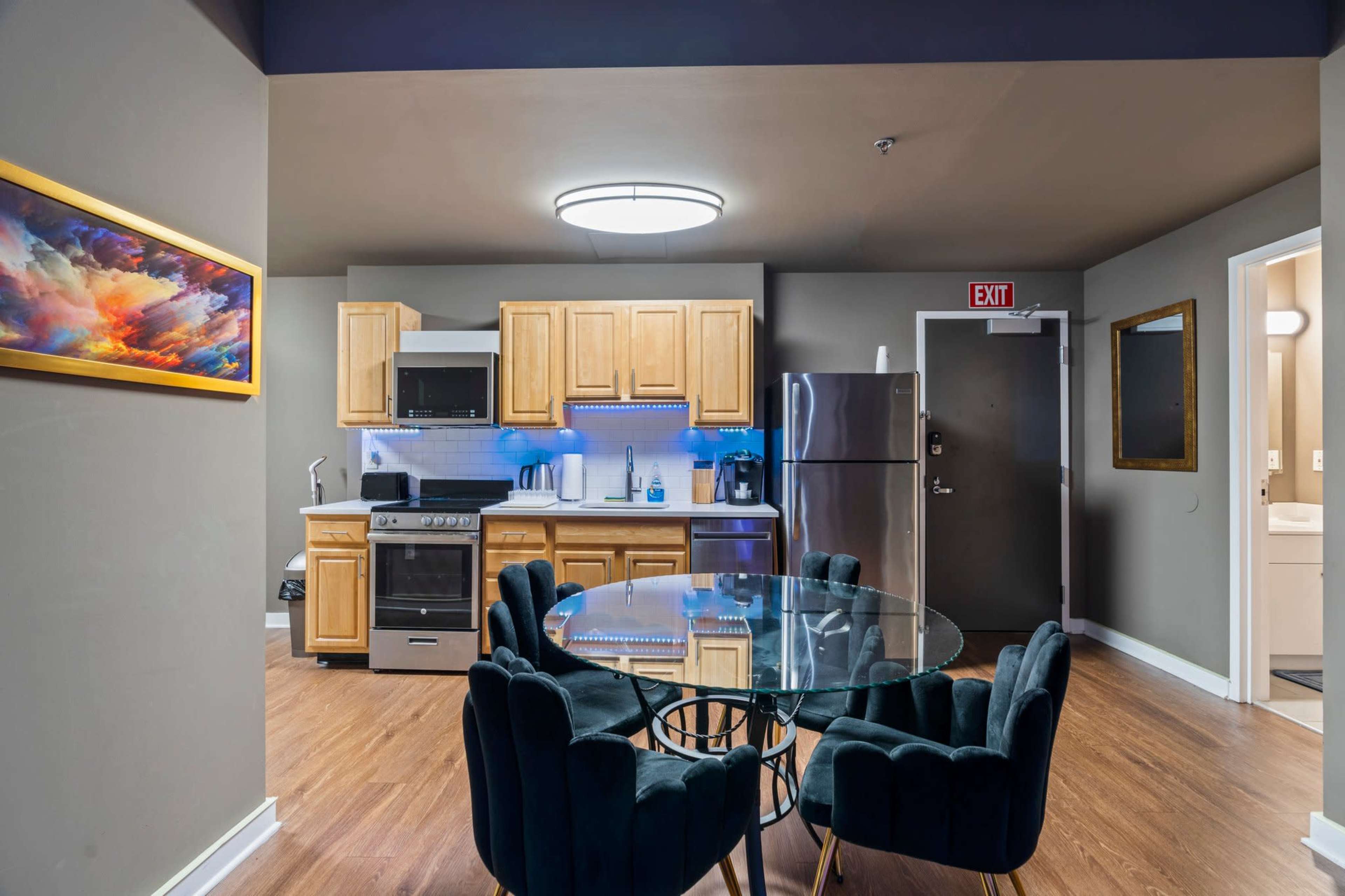 A kitchen area with wooden cabinets, an oven, a microwave, and a glass dining table surrounded by black chairs.