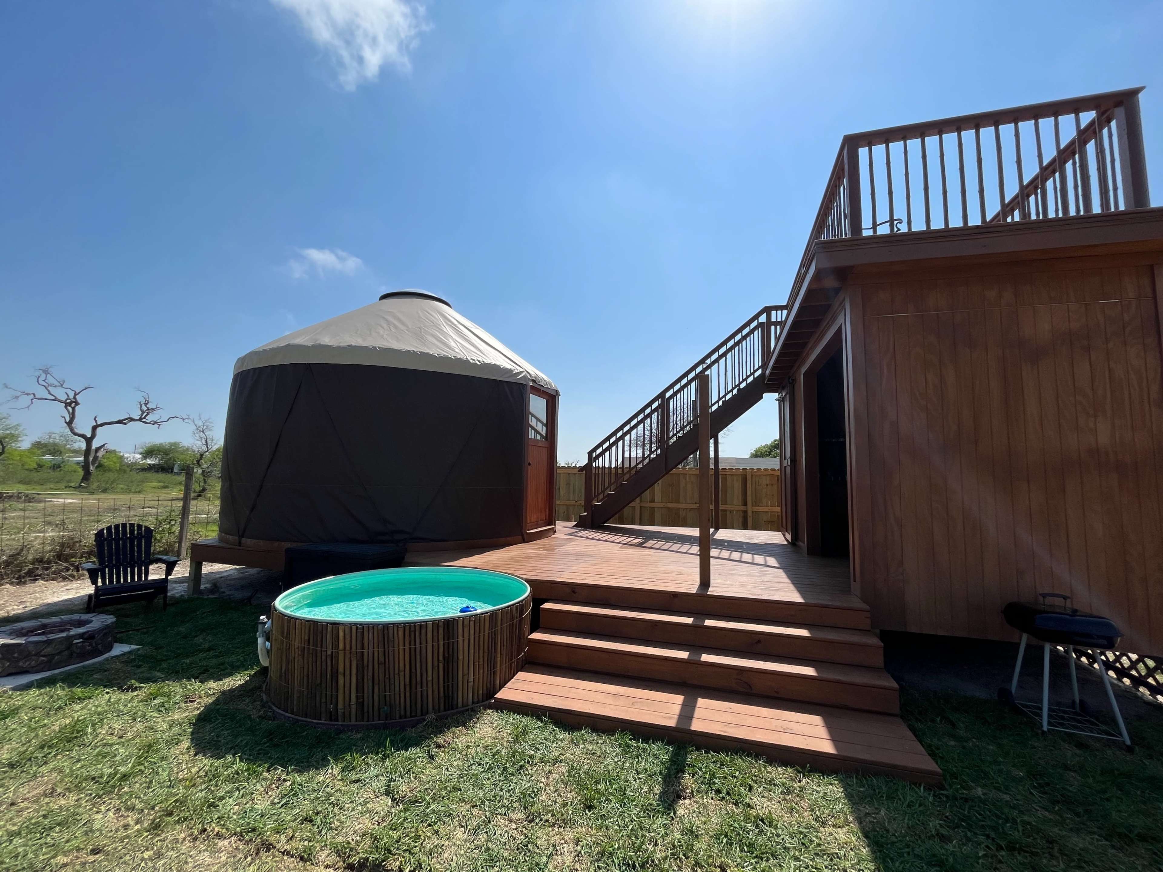 A wooden deck leads to a round yurt and a small above-ground pool in a grassy outdoor setting.