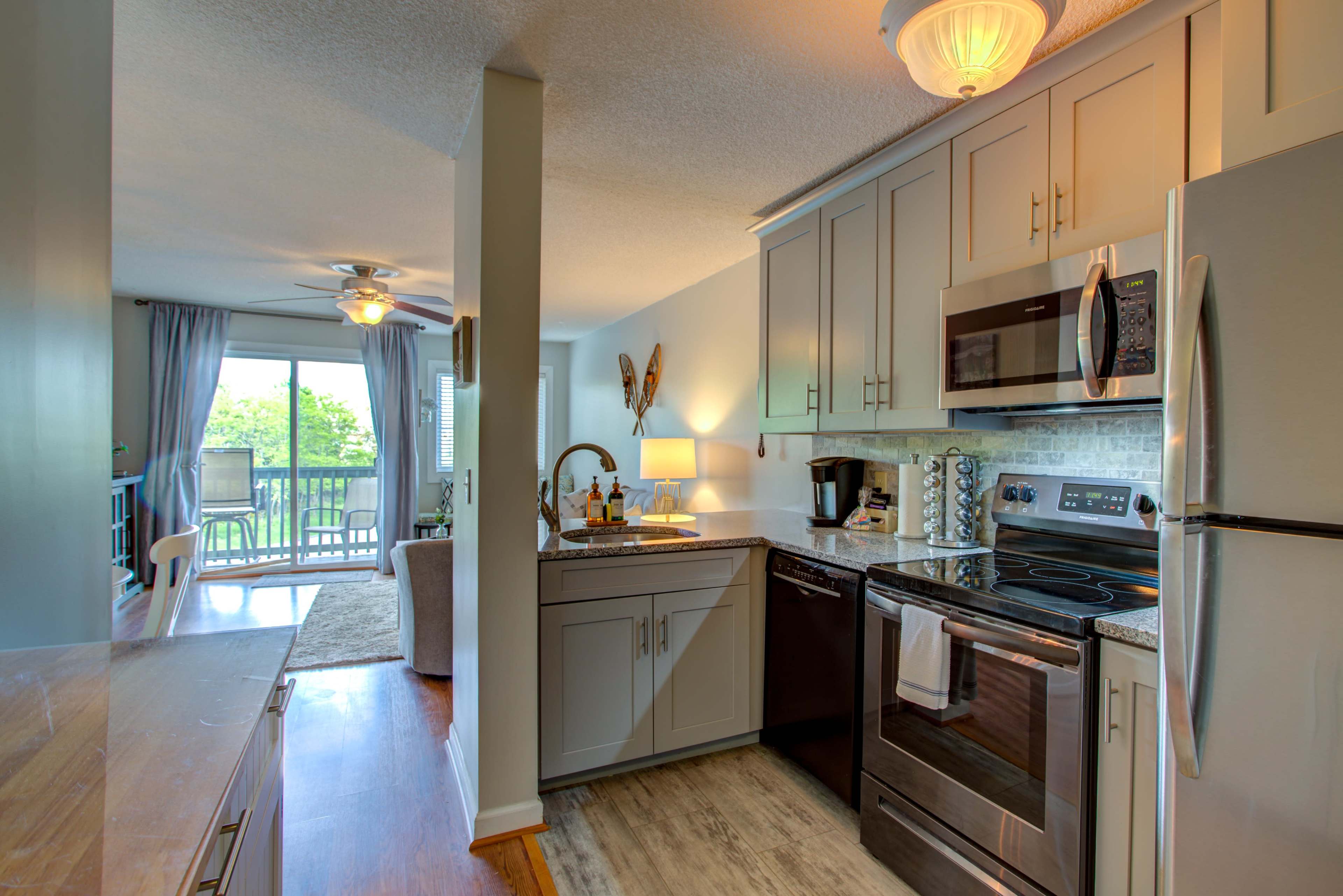 A modern kitchen features stainless steel appliances and a view of a balcony through an open living area.