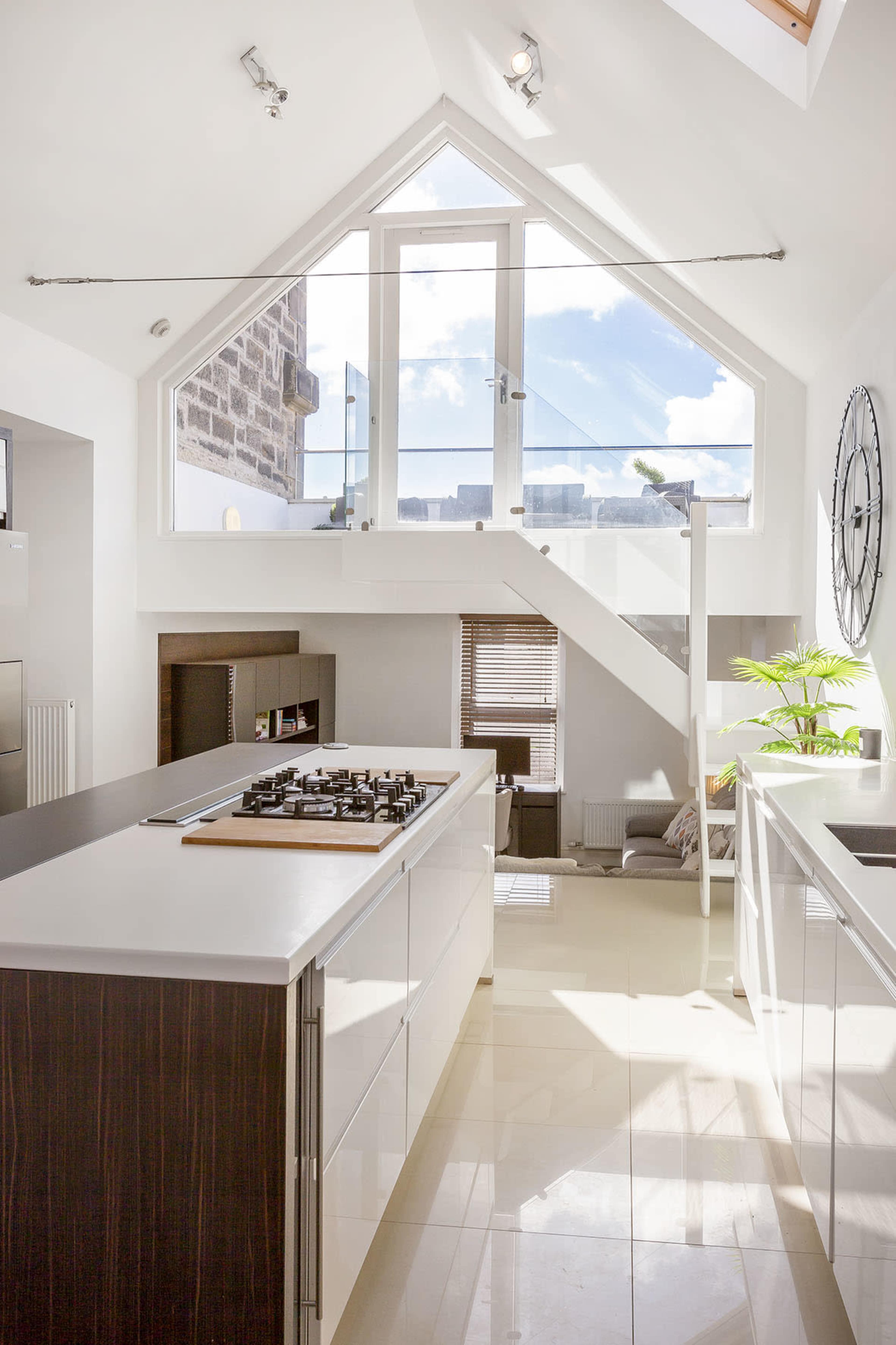 A modern kitchen with a triangular window above a sleek countertop and a staircase leading to an upper level.