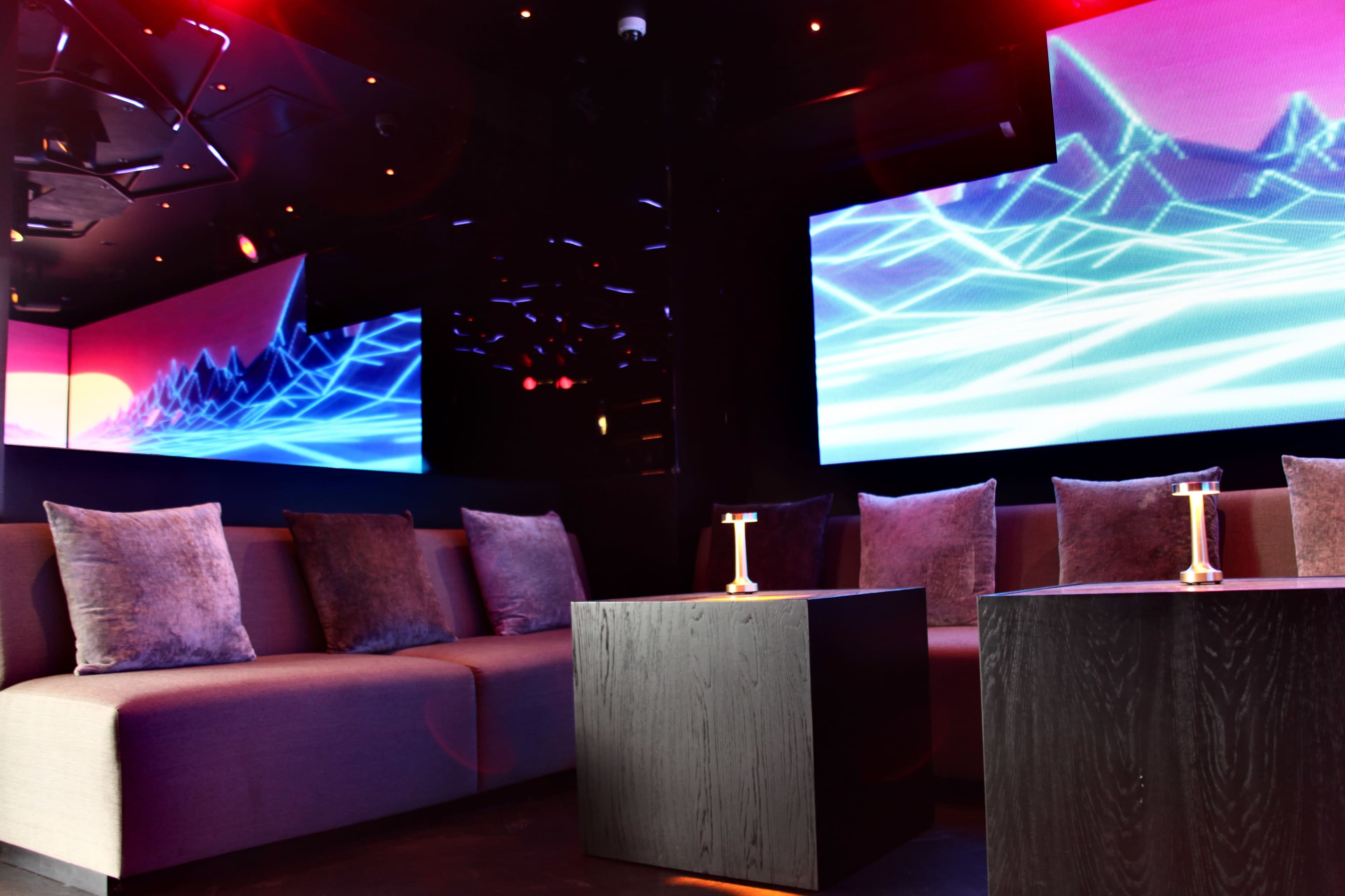 A modern lounge area with plush seating and large screens displaying abstract graphics.