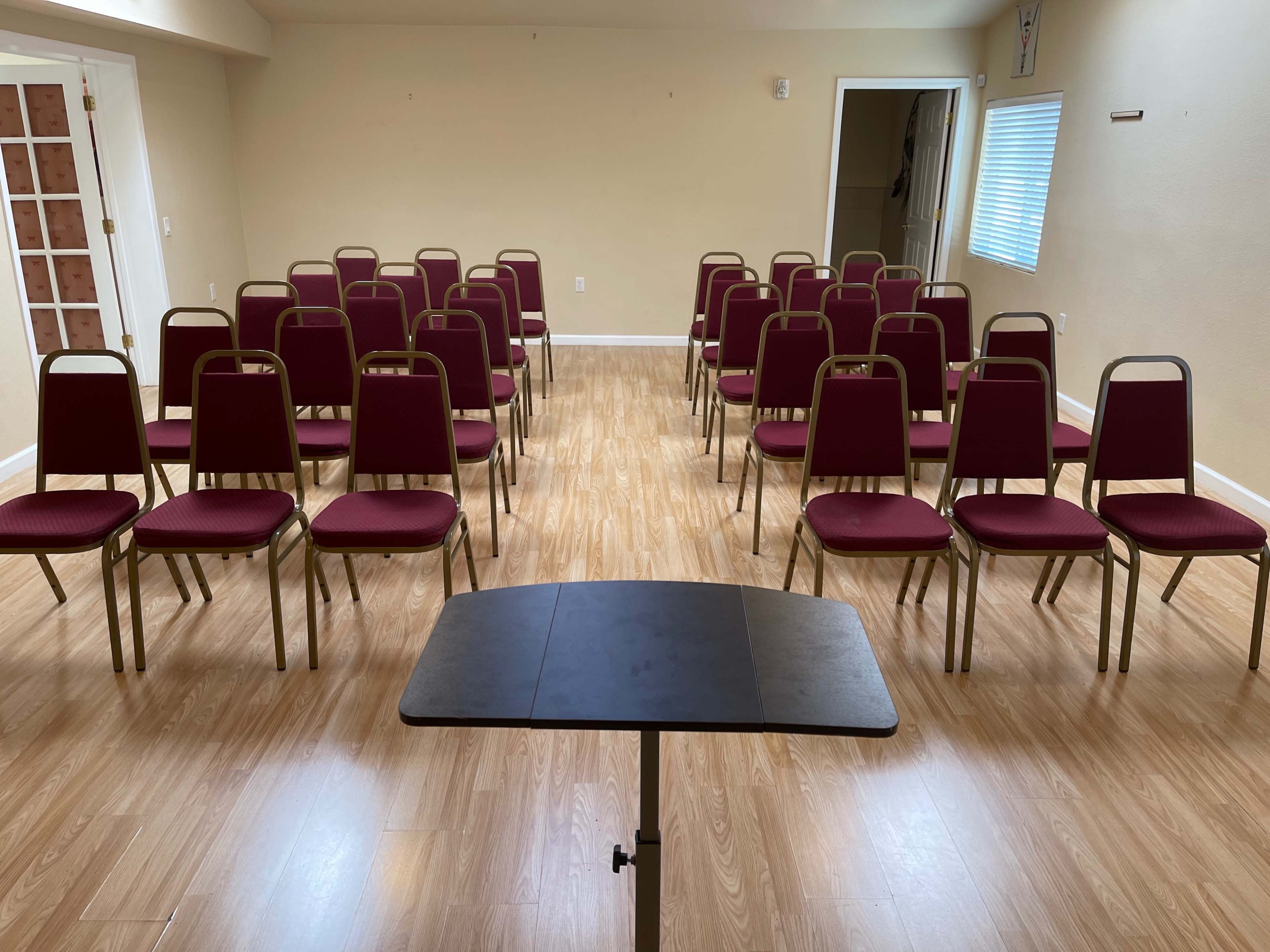A room set up with rows of maroon chairs facing a small black table in the center.