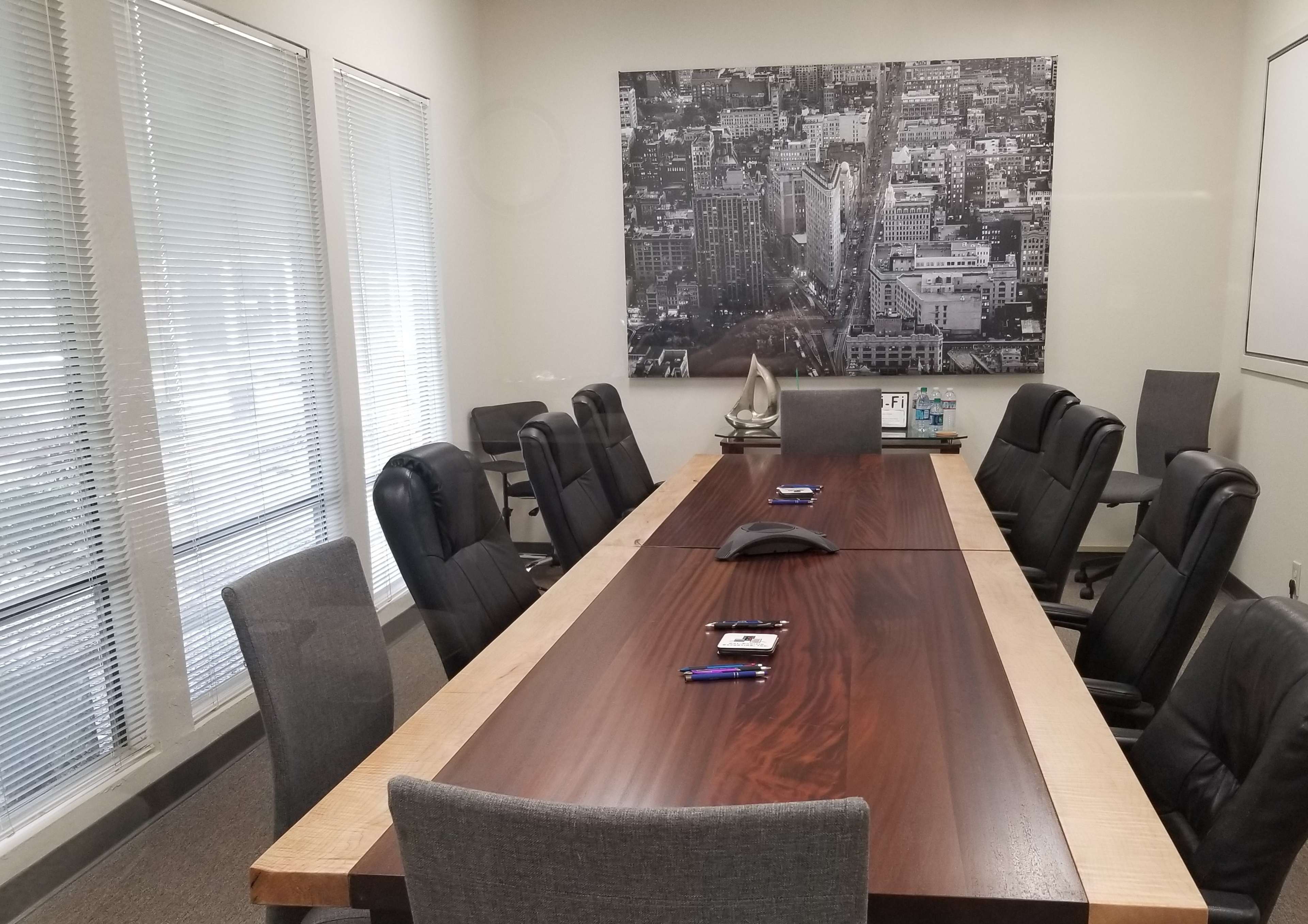 A conference room features a large wooden table surrounded by office chairs and a black-and-white cityscape photograph on the wall.