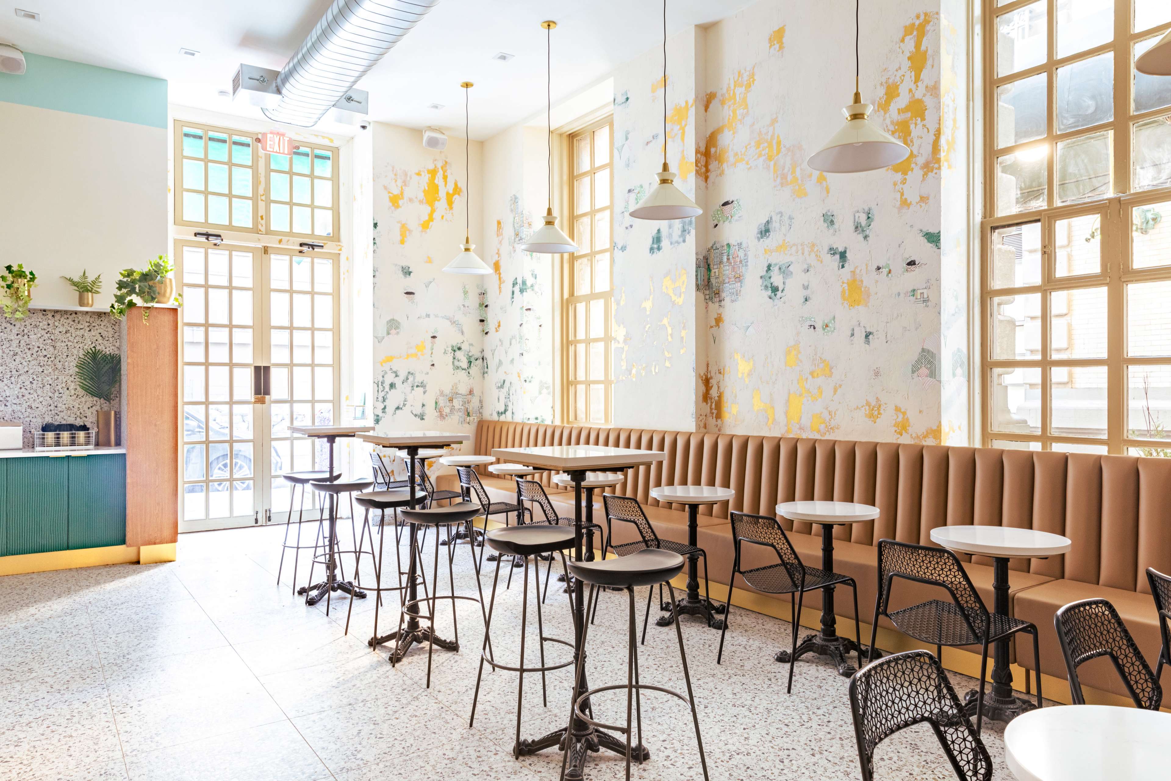 A bright café interior with a mix of brown upholstered seating, round tables, and large windows allowing natural light to enter.