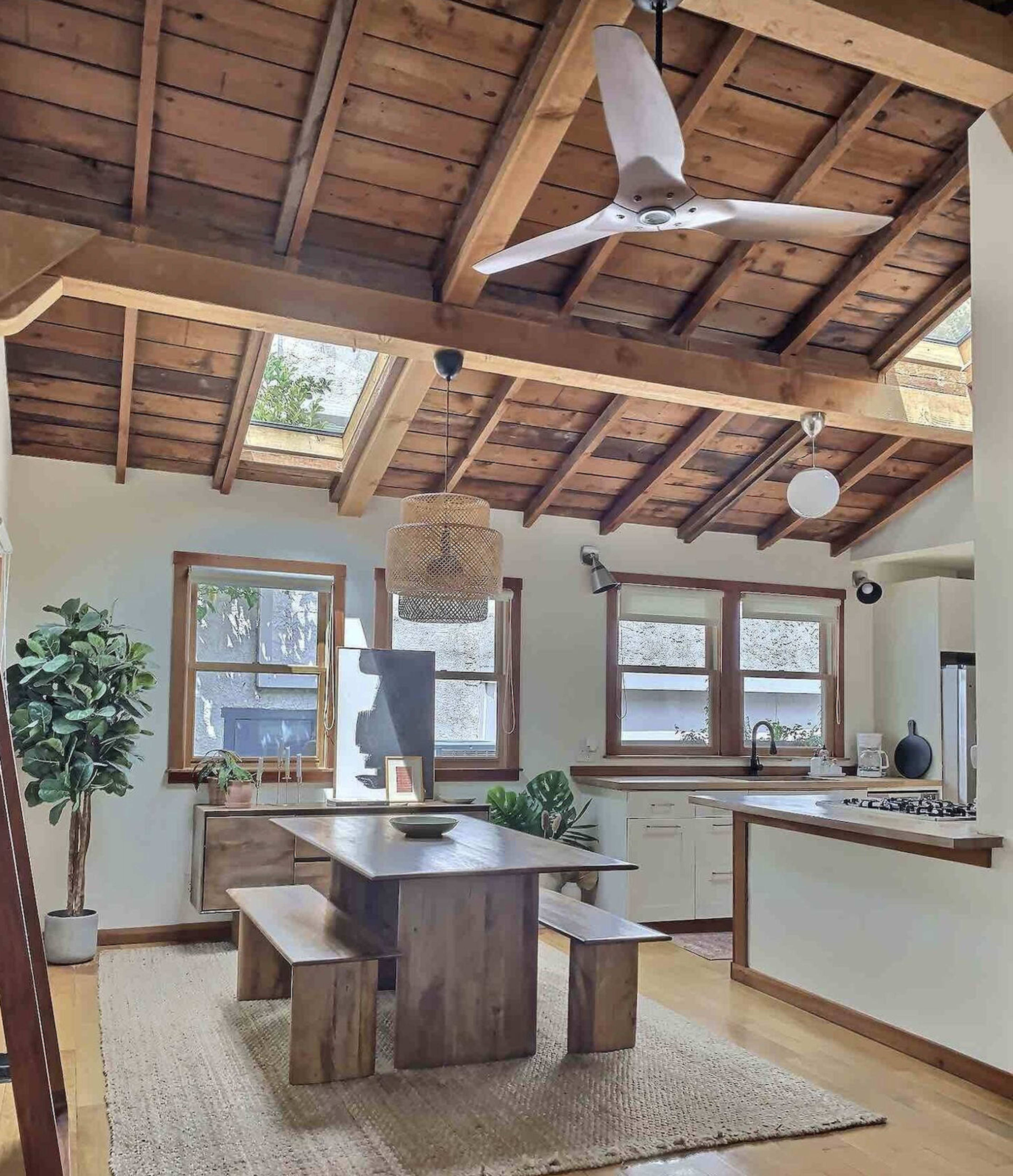 A modern kitchen and dining area with wooden beams, a large table, and a mixture of natural and artificial lighting.
