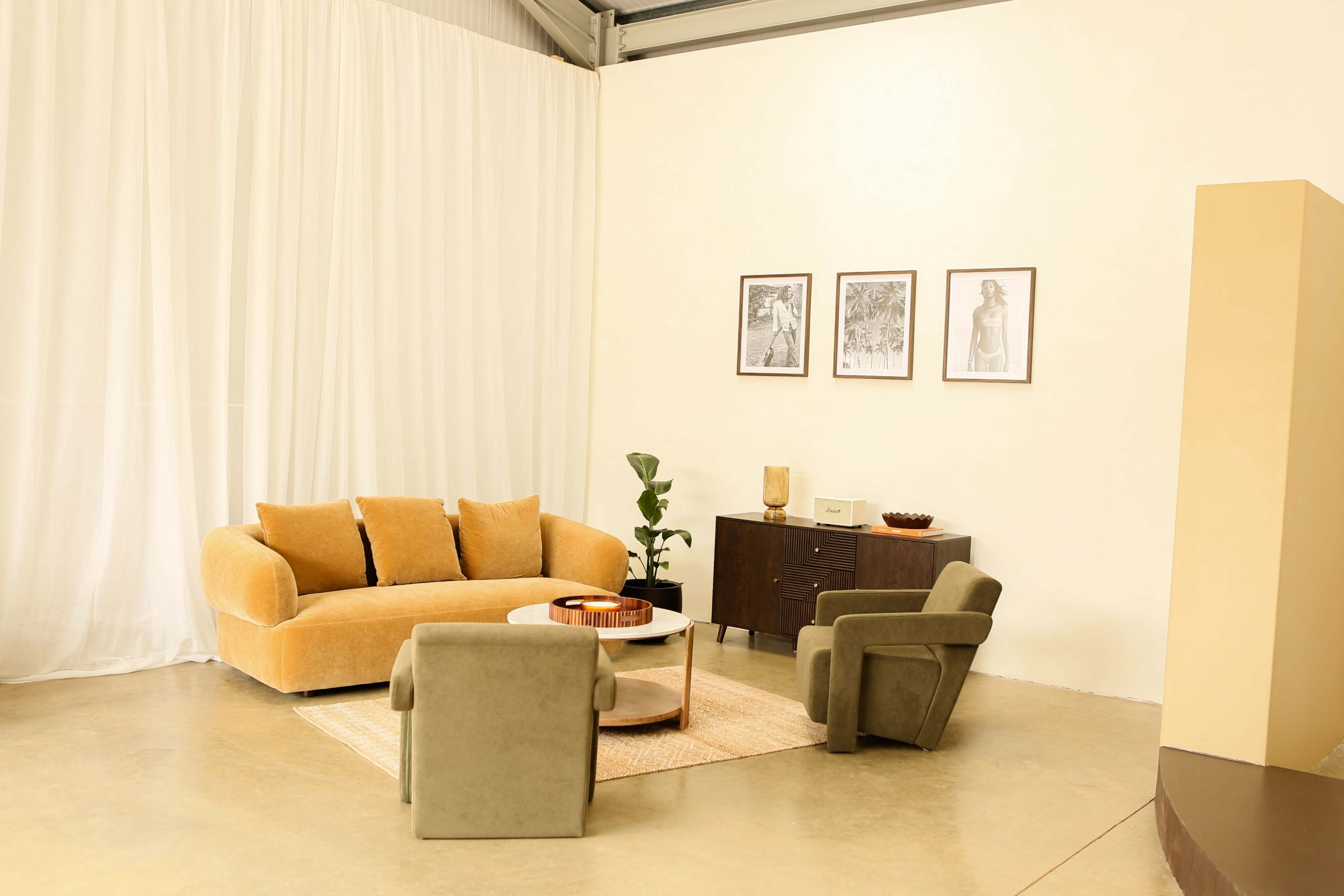 The image shows a modern living room with a yellow sofa, two green armchairs, a round coffee table, and framed artwork on the wall.