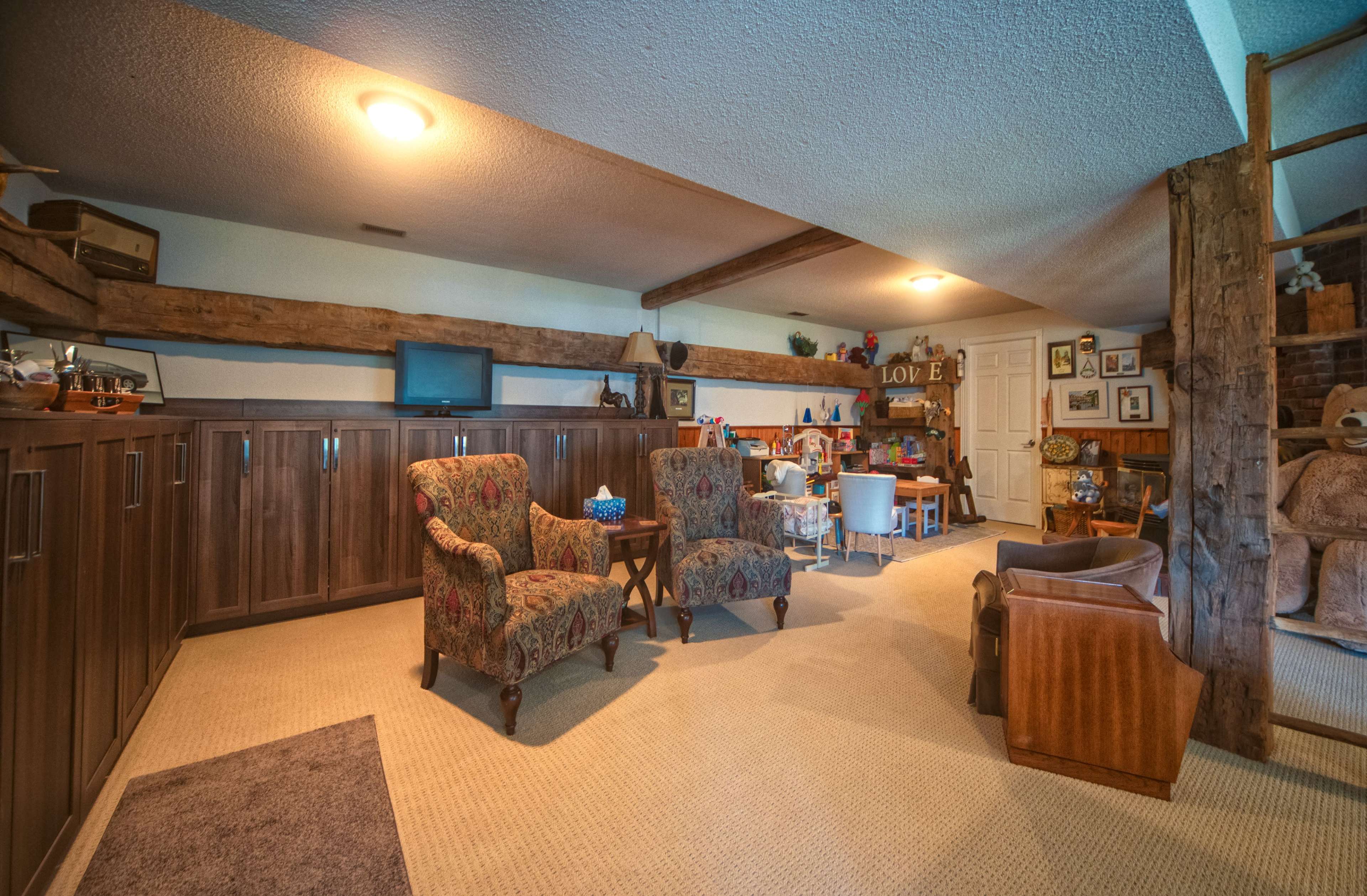 The image shows a finished basement living area with two upholstered chairs, a coffee table, and various shelves and decor against the walls.