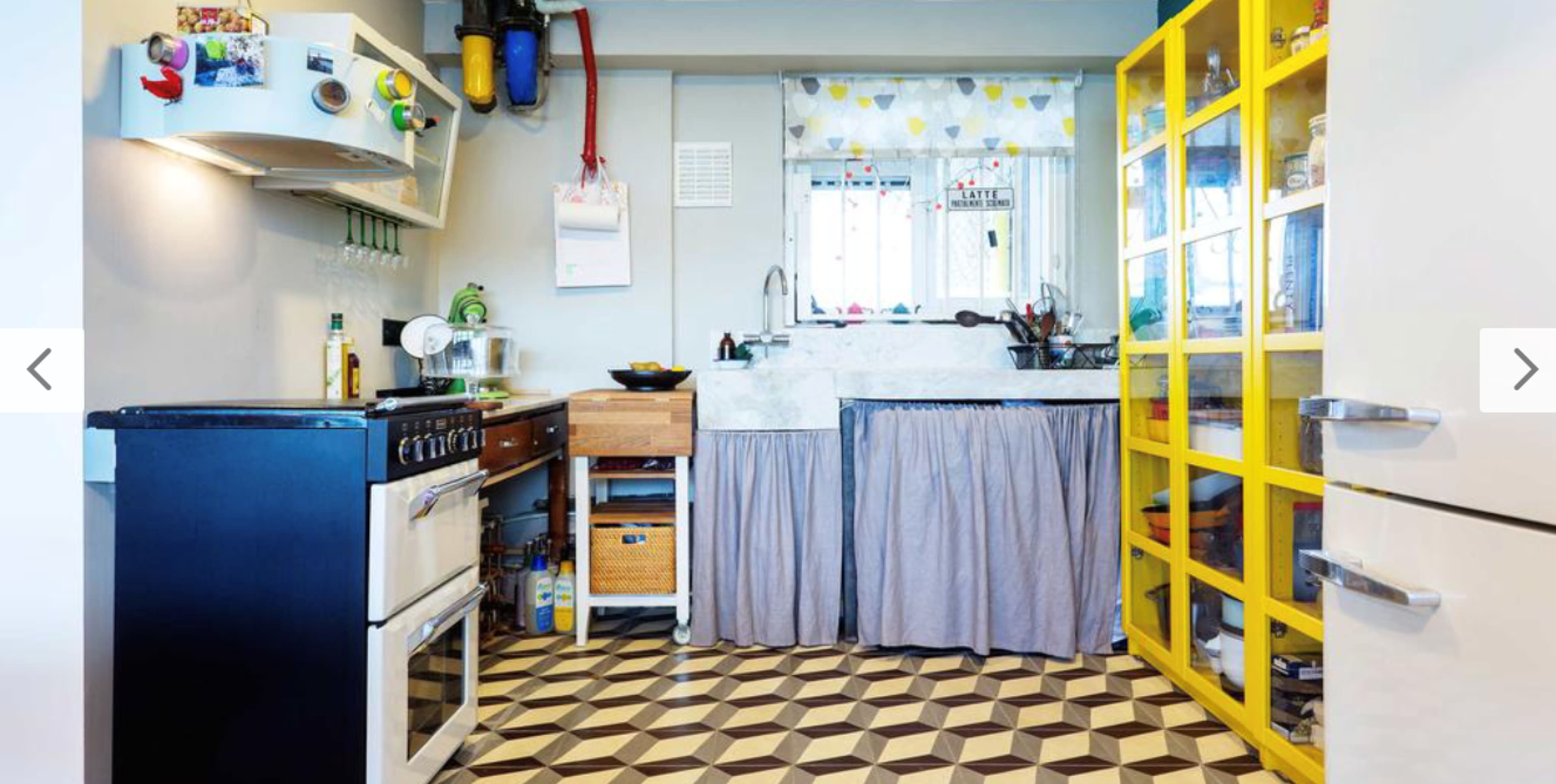 A compact kitchen featuring a two-tone color scheme with a black stove, a wooden storage unit, a marble countertop, and a bright yellow glass-door cabinet.