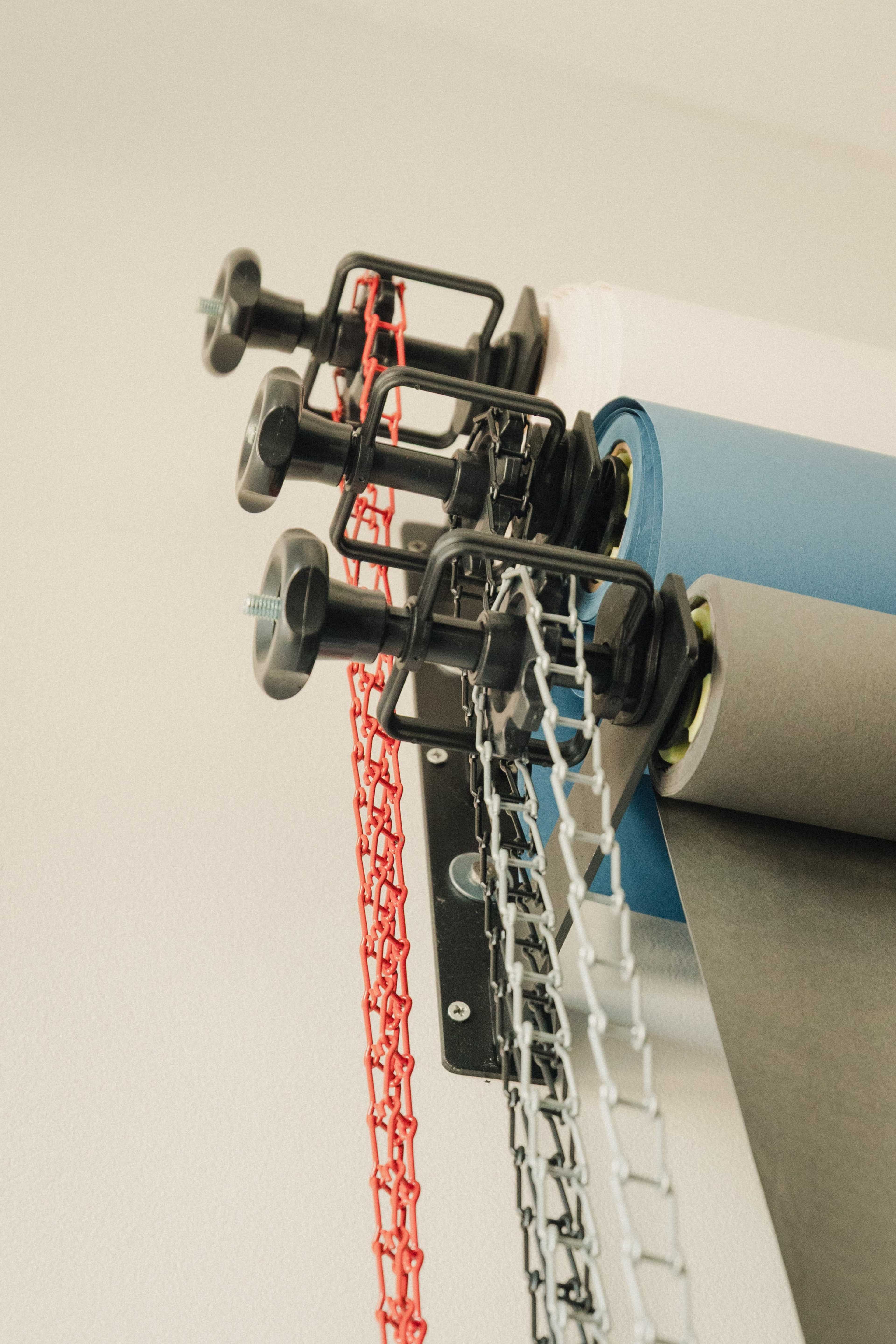 The image shows three rolls of colored paper mounted on a wall, secured by adjustable clamps.