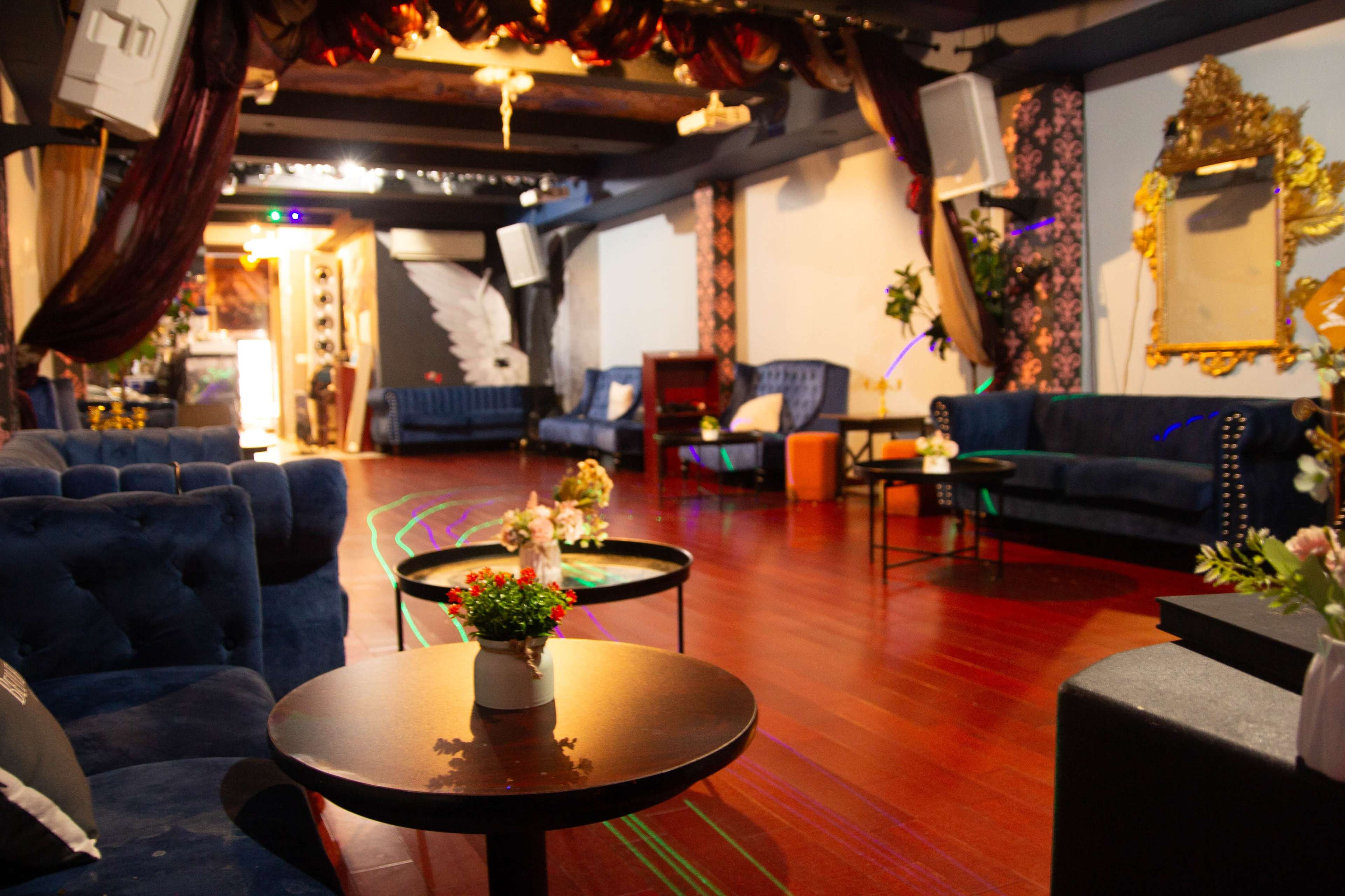 The image shows a spacious lounge area with dark blue couches, small tables, and decorative lighting.