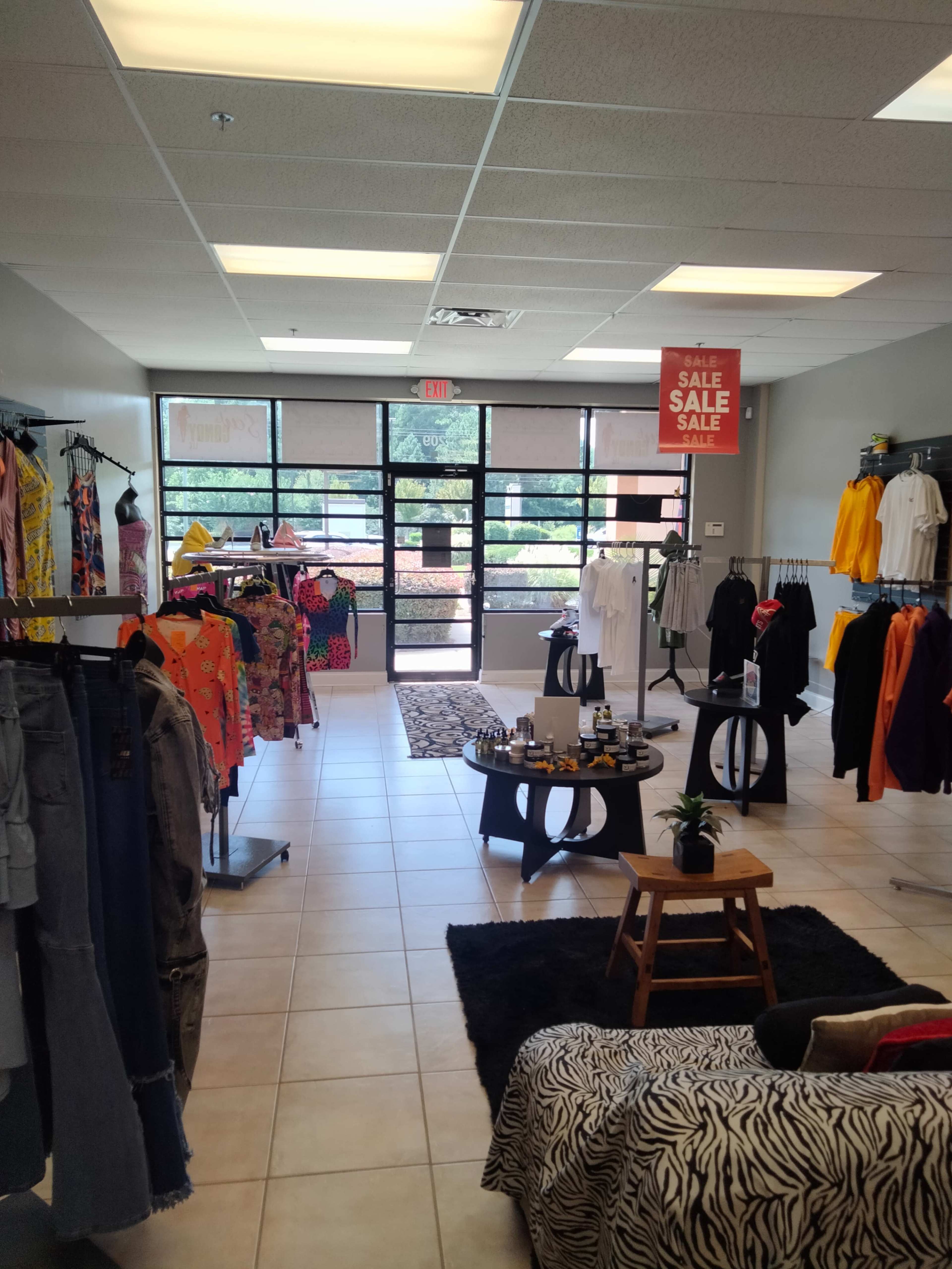 A clothing store interior with racks of colorful apparel, a display table with products, and large front windows allowing natural light to enter.