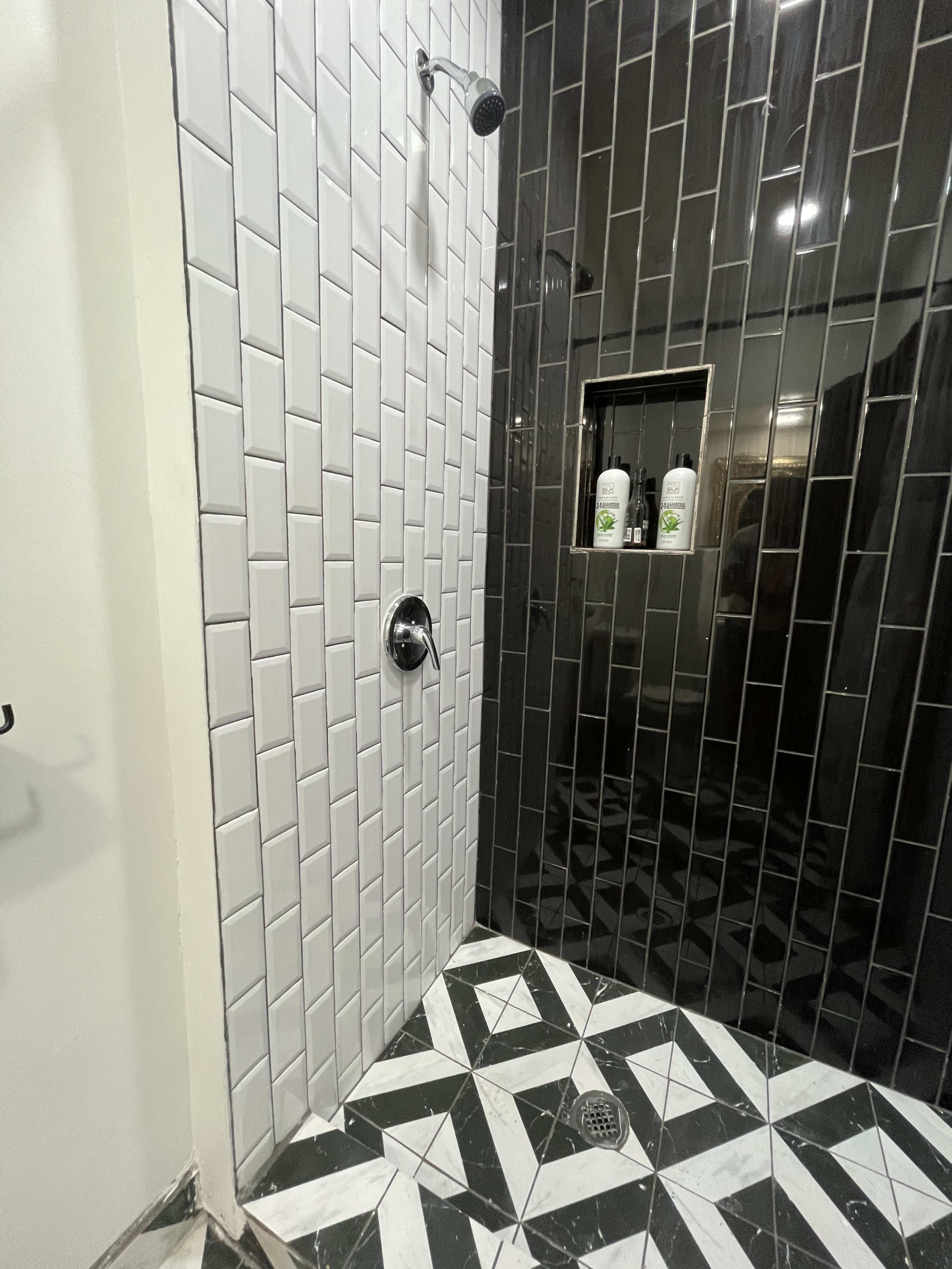 A modern shower area with a mix of black and white tiled walls and a patterned floor.