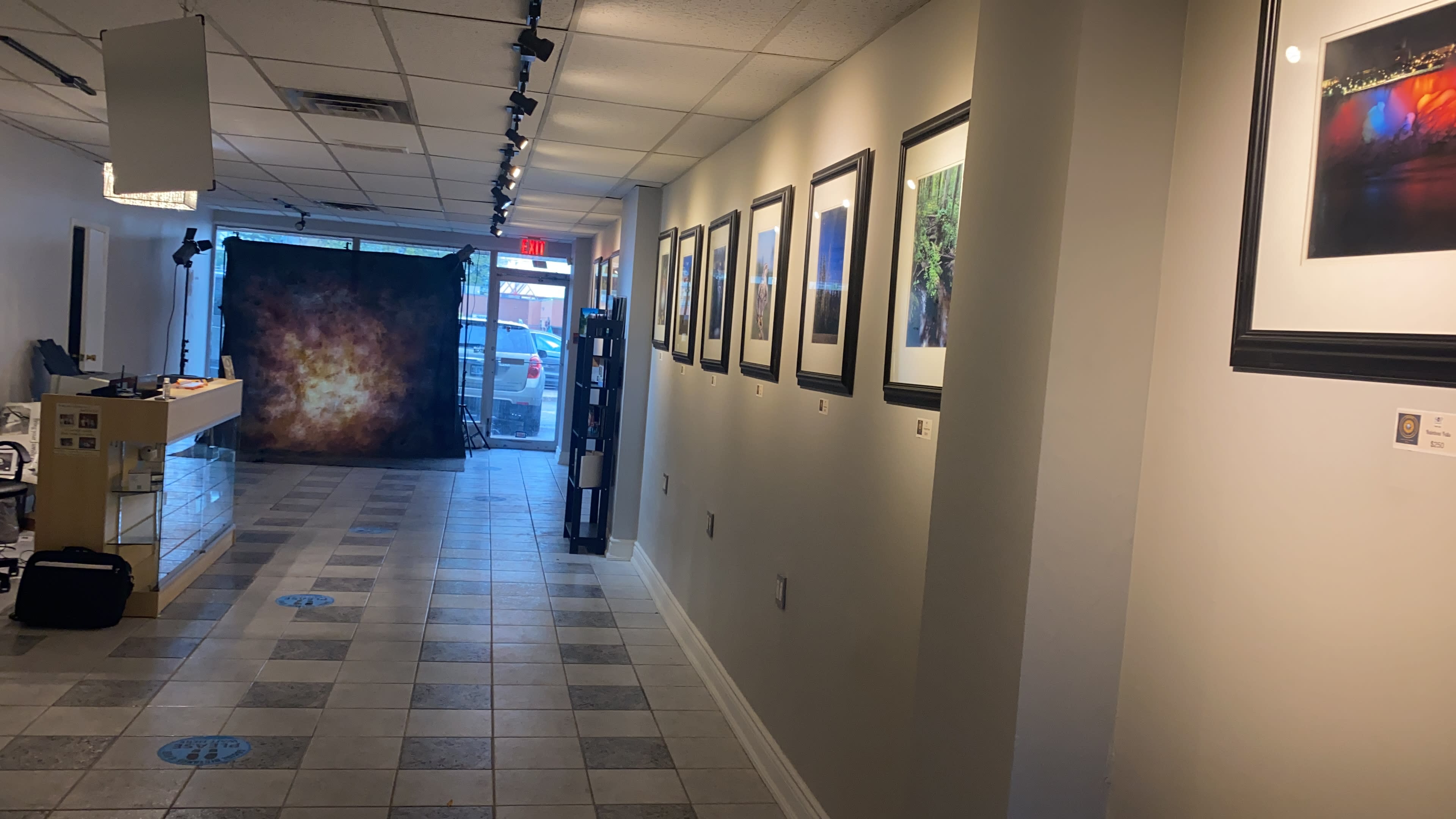 A long corridor in an art gallery with framed photographs on the walls and a backdrop for photography at the end.