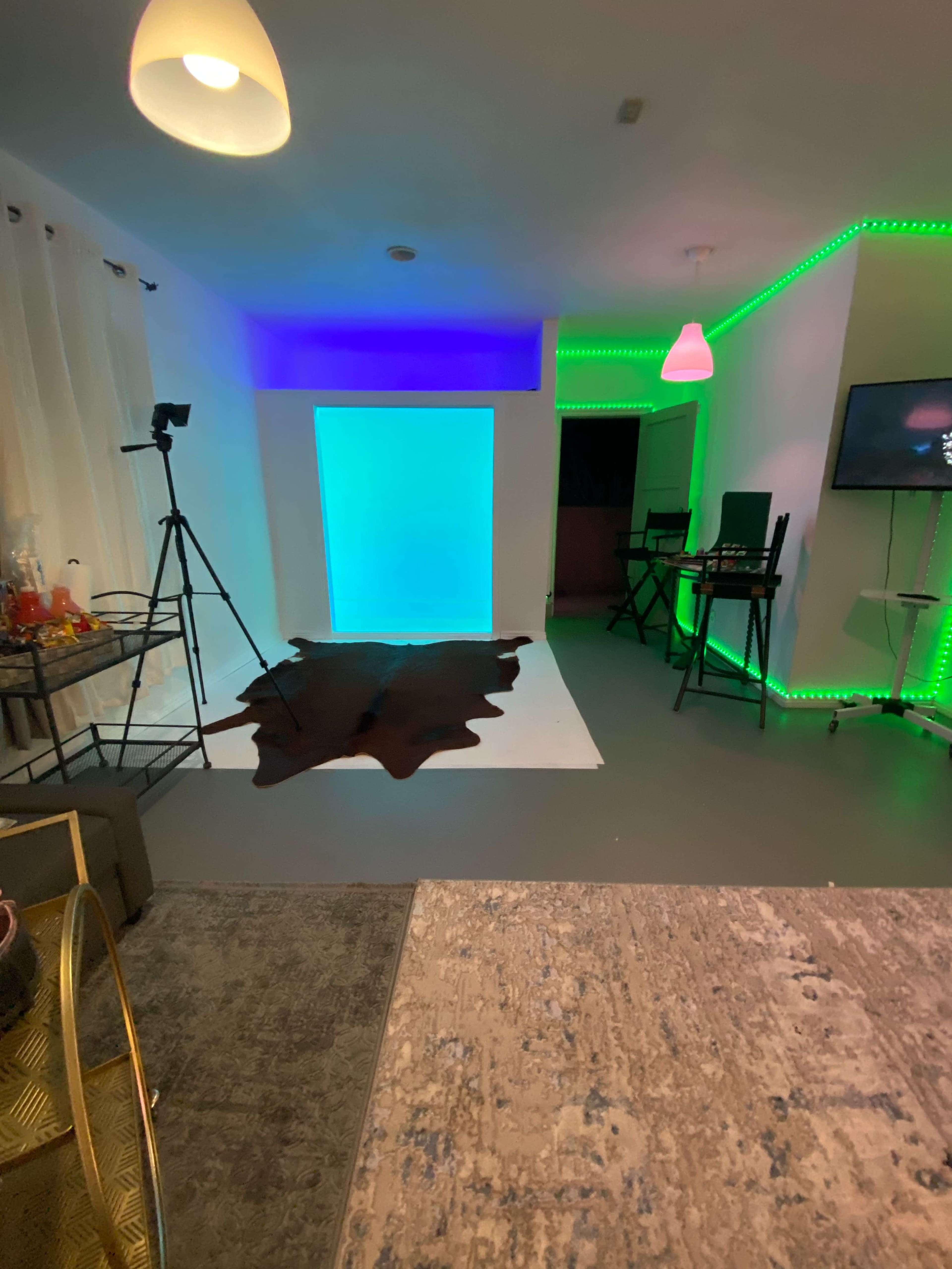 A modern studio space with a green and blue lit backdrop, a black cowhide rug on the floor, and various equipment set up for photography or videography.