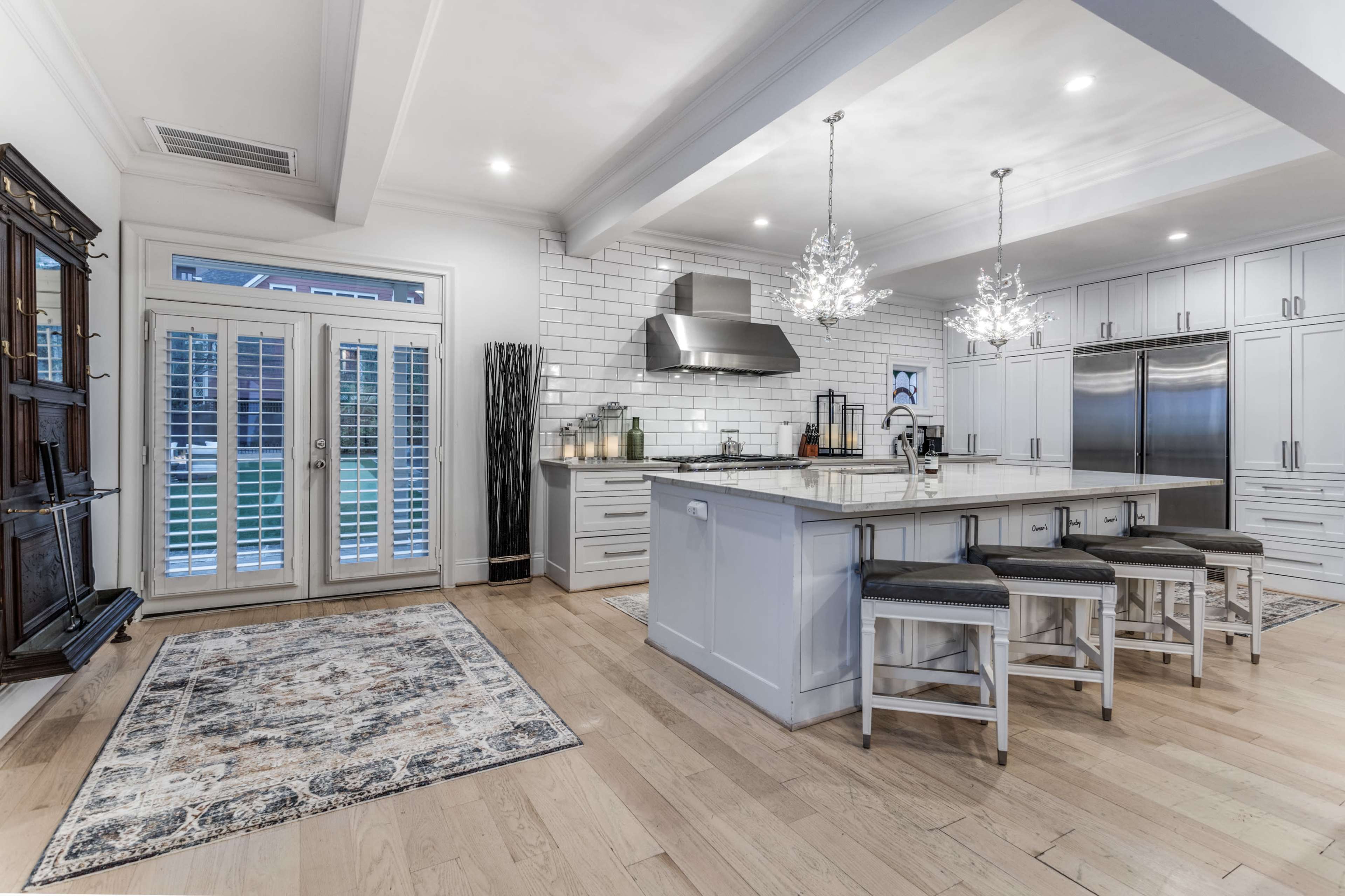 A modern kitchen with a large island, stainless steel appliances, a tile backsplash, and double doors leading to an outdoor area.