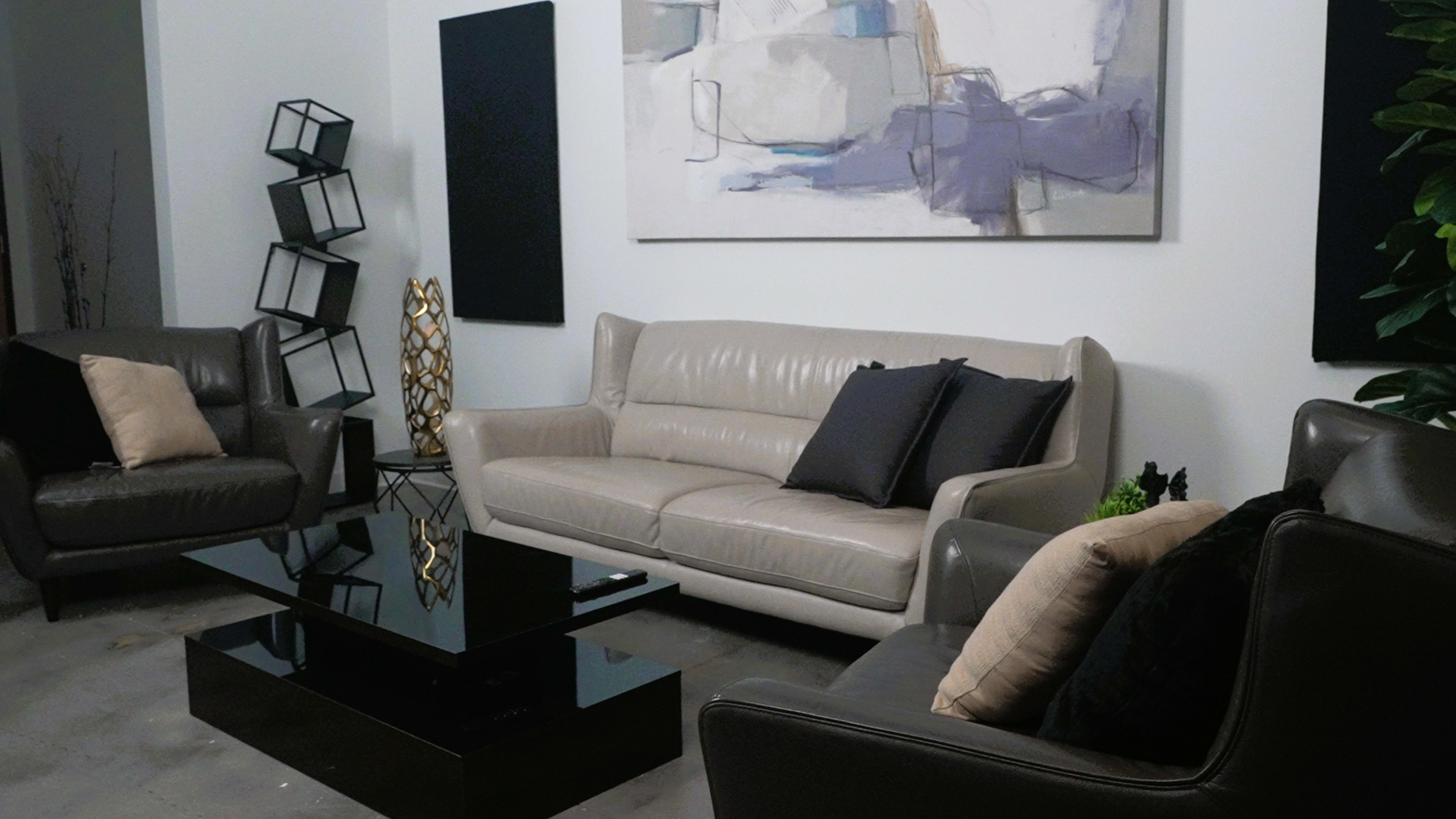 The image depicts a modern living room with a light-colored leather sofa, two armchairs, a black coffee table, and abstract artwork on the wall.