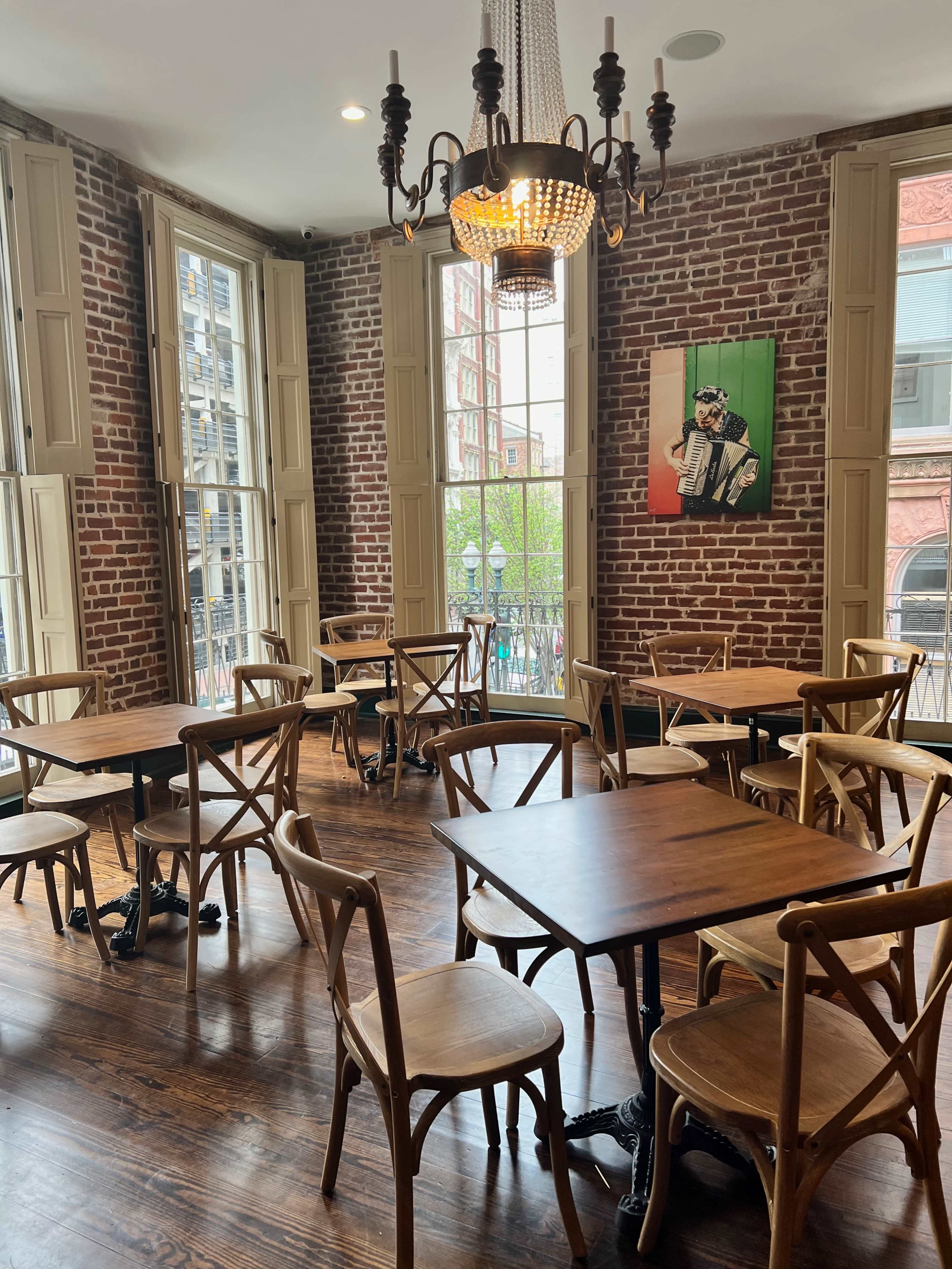 The image shows a cozy restaurant interior with wooden tables and chairs, exposed brick walls, large windows, and a chandelier.