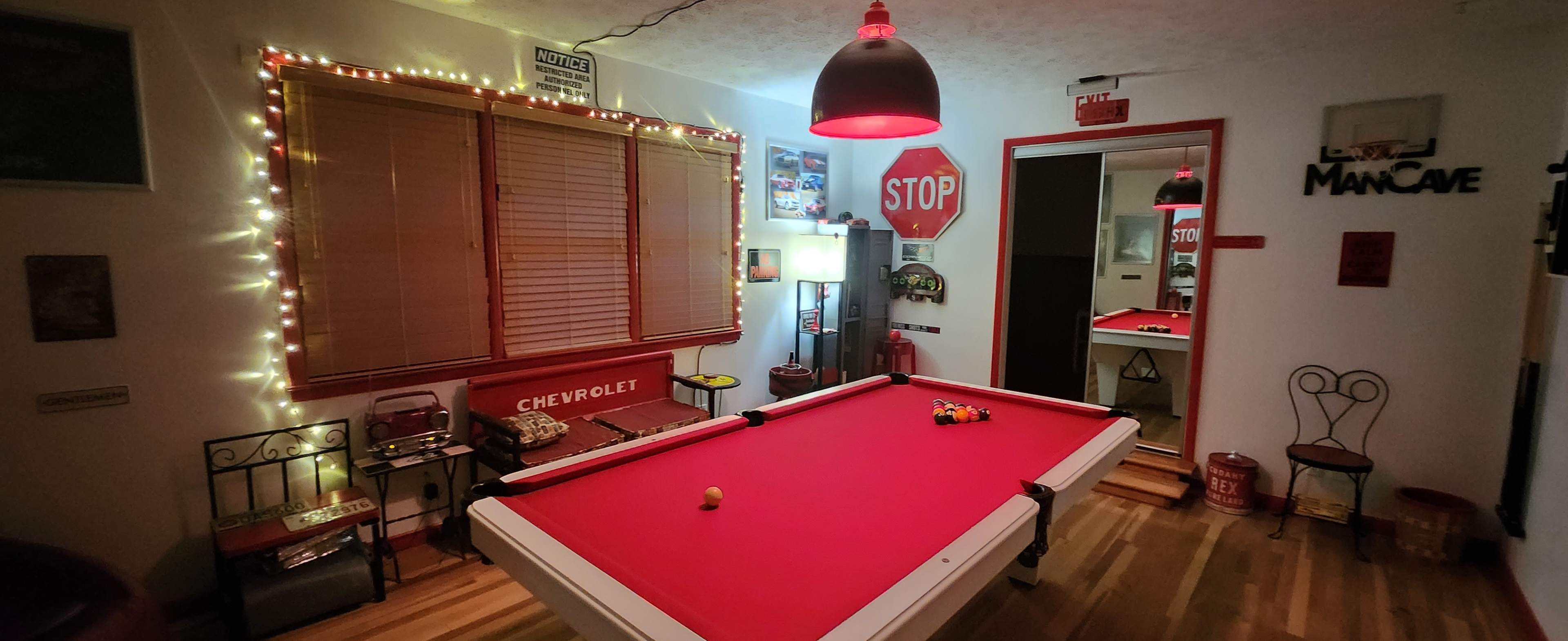 The image shows a game room featuring a red pool table, a stop sign, and various decorations, with warm lighting and a mirror reflecting part of the space.