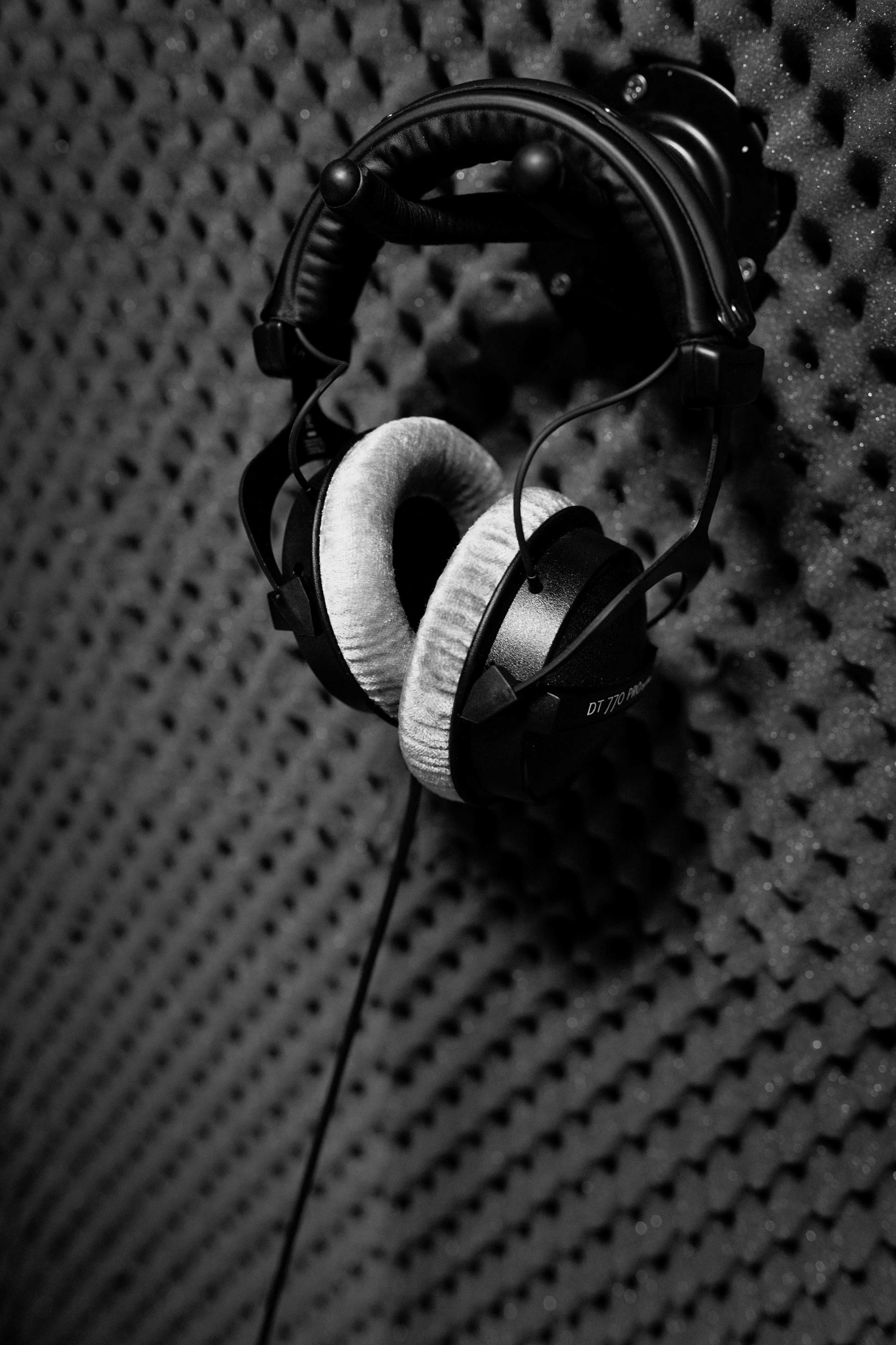 A pair of black headphones hangs against a textured soundproof wall.