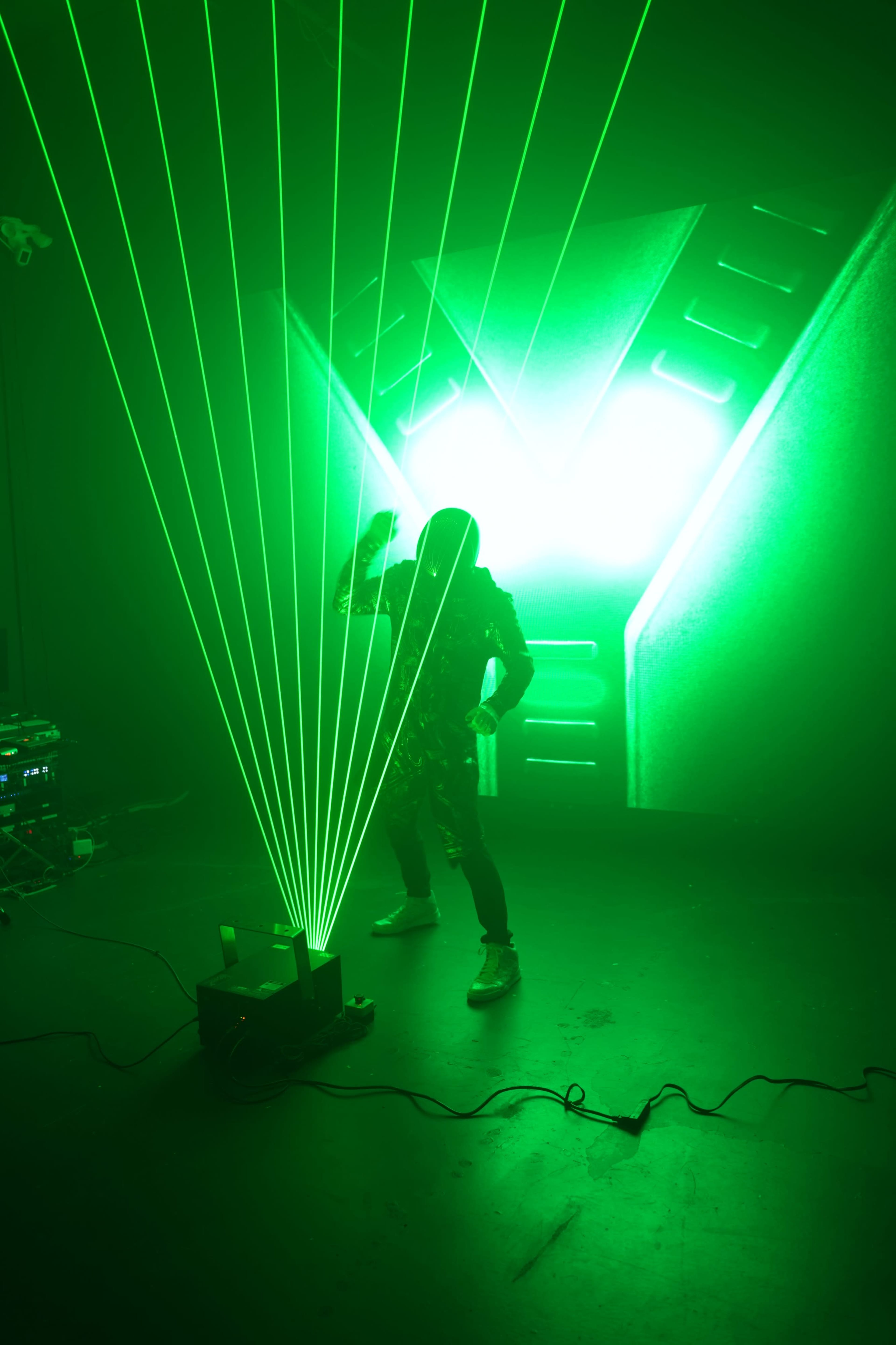 A person stands in a dark room surrounded by vibrant green laser beams emanating from a projector.
