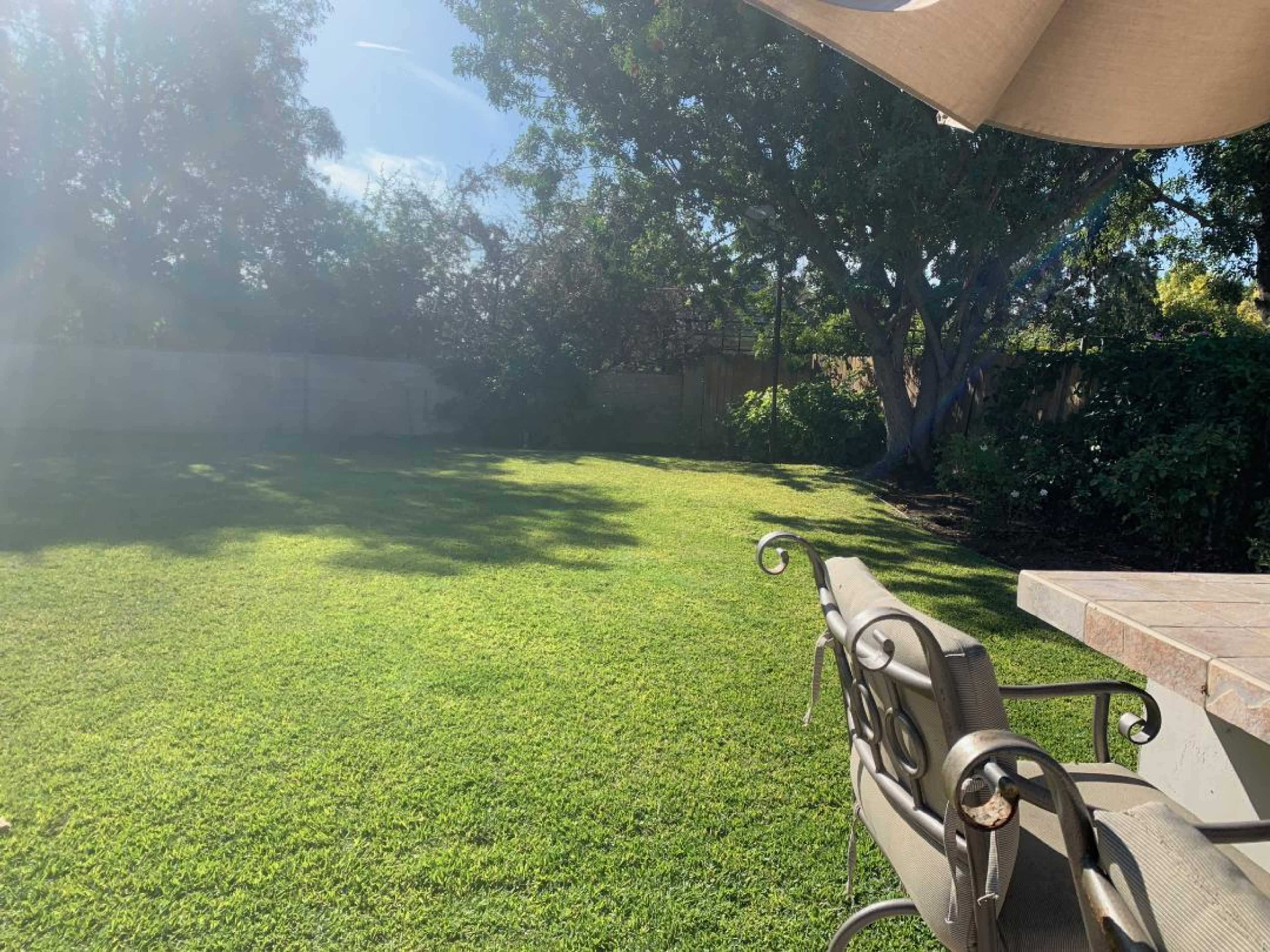 A well-maintained backyard features a large expanse of green grass, with a shaded area provided by a patio umbrella.