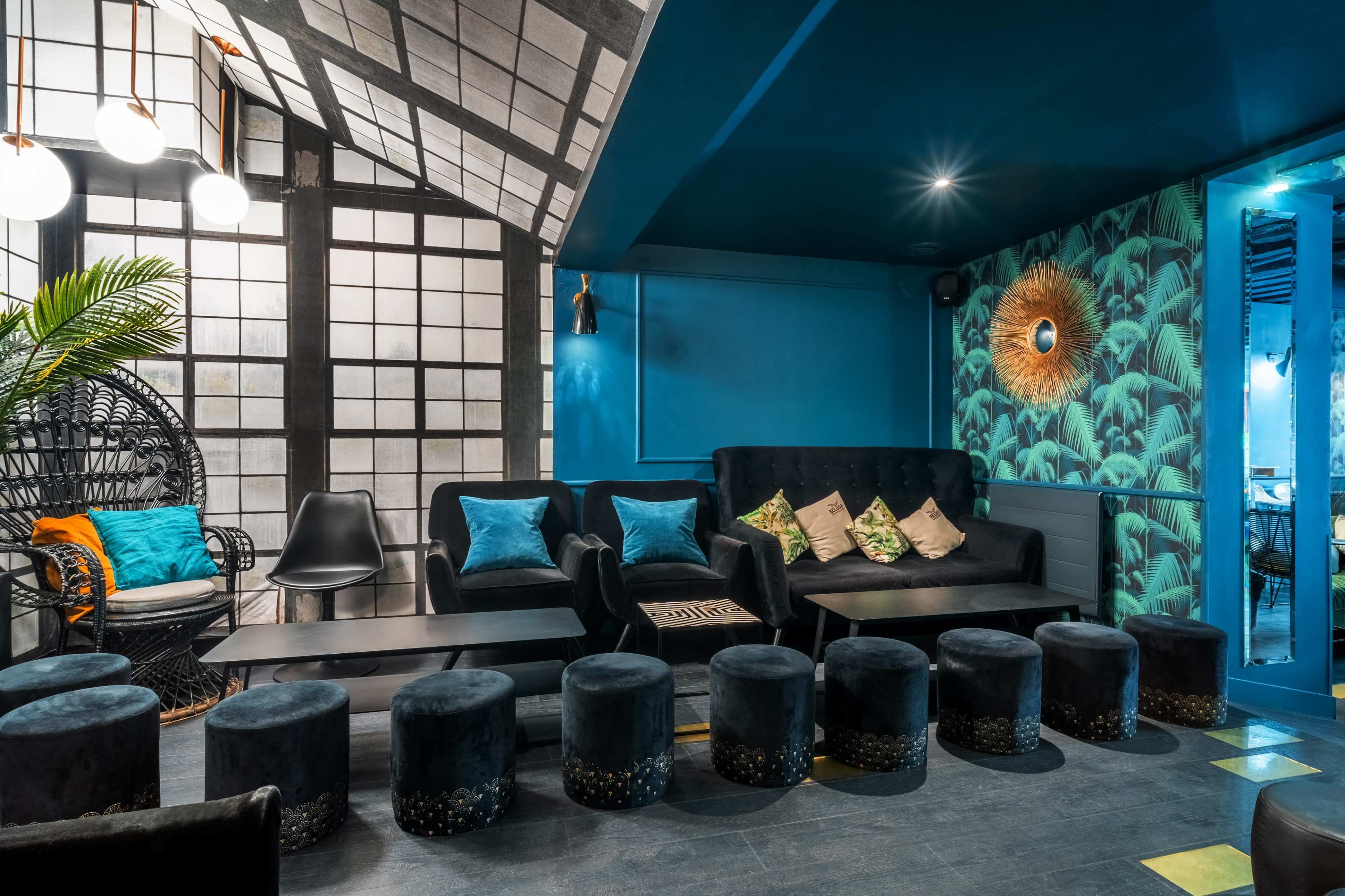 A modern lounge area with dark blue walls, a mix of upholstered seating, and a decorative wall featuring large tropical leaves.